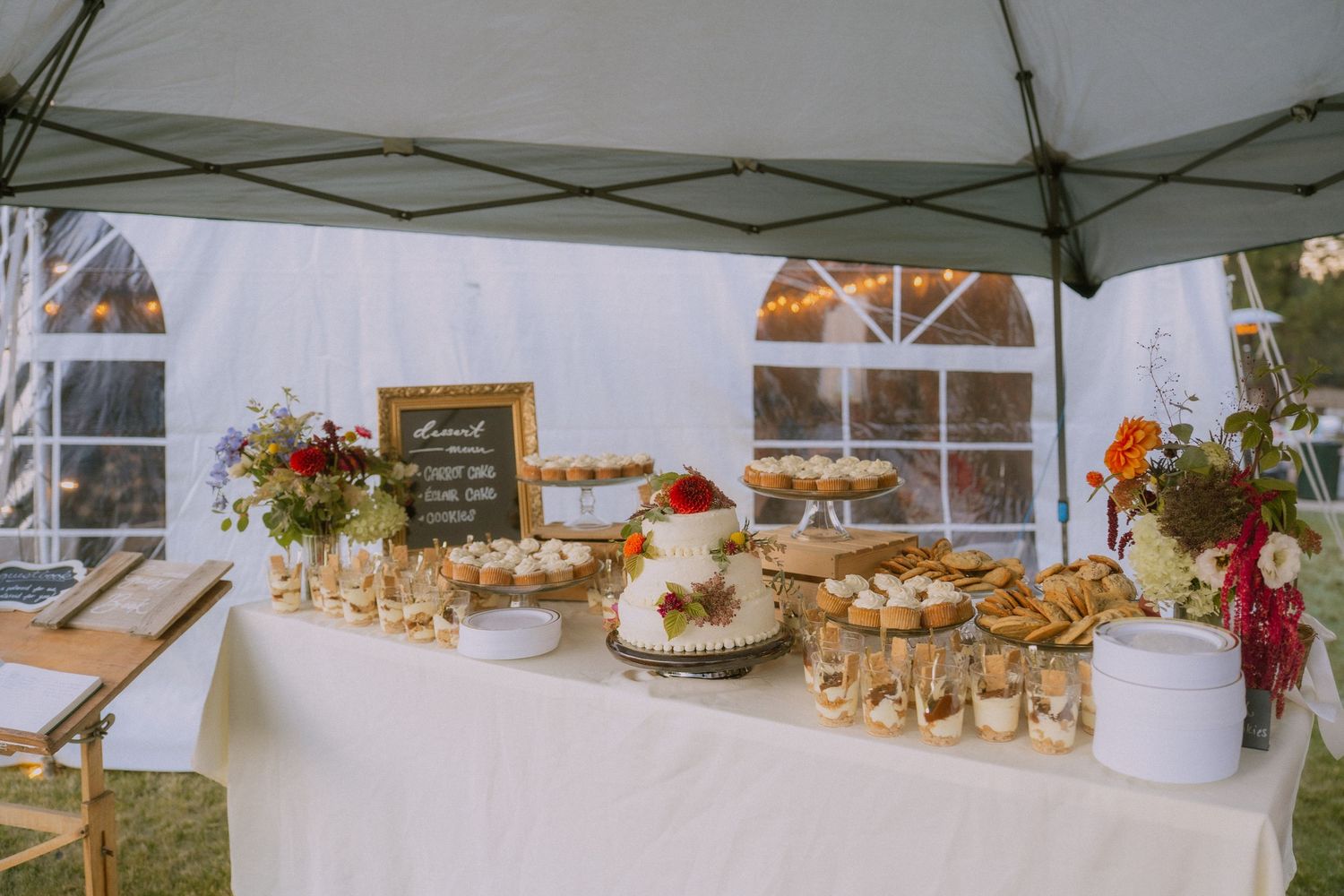 A wedding reception setup under a white tent with rustic decor and floral arrangements on tables.