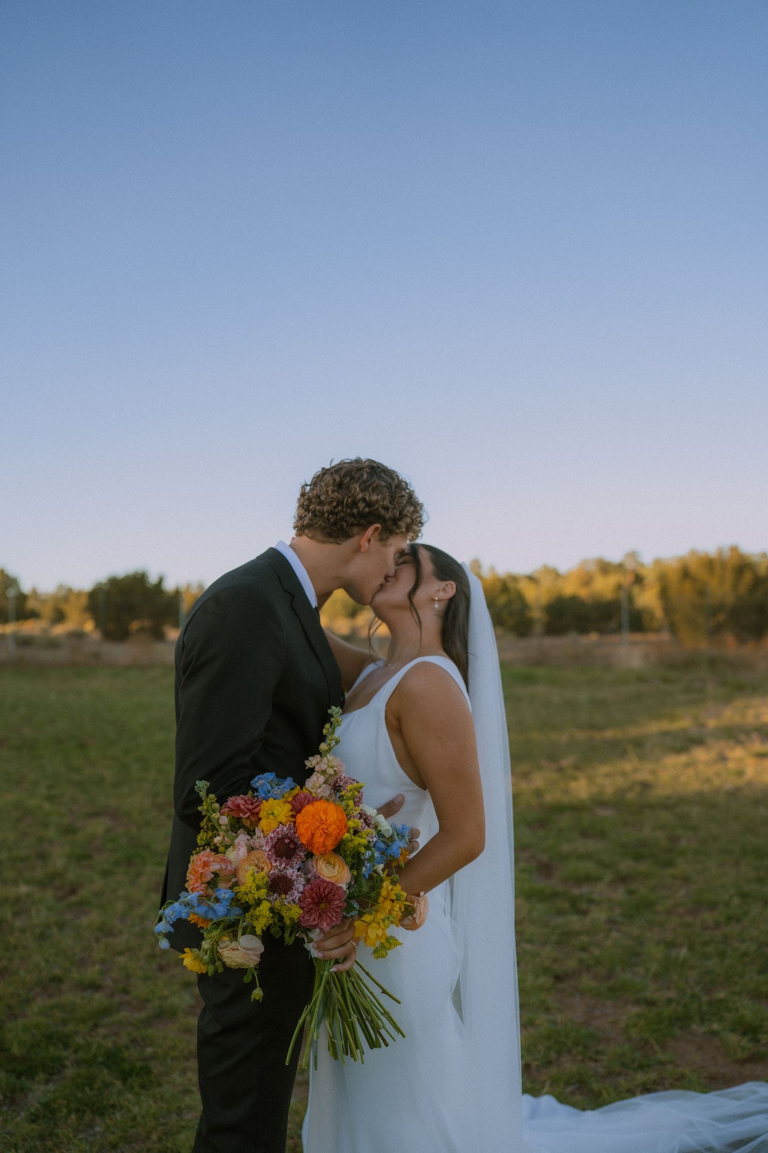 A romantic wedding moment captured in a golden field with a vibrant wildflower bouquet.