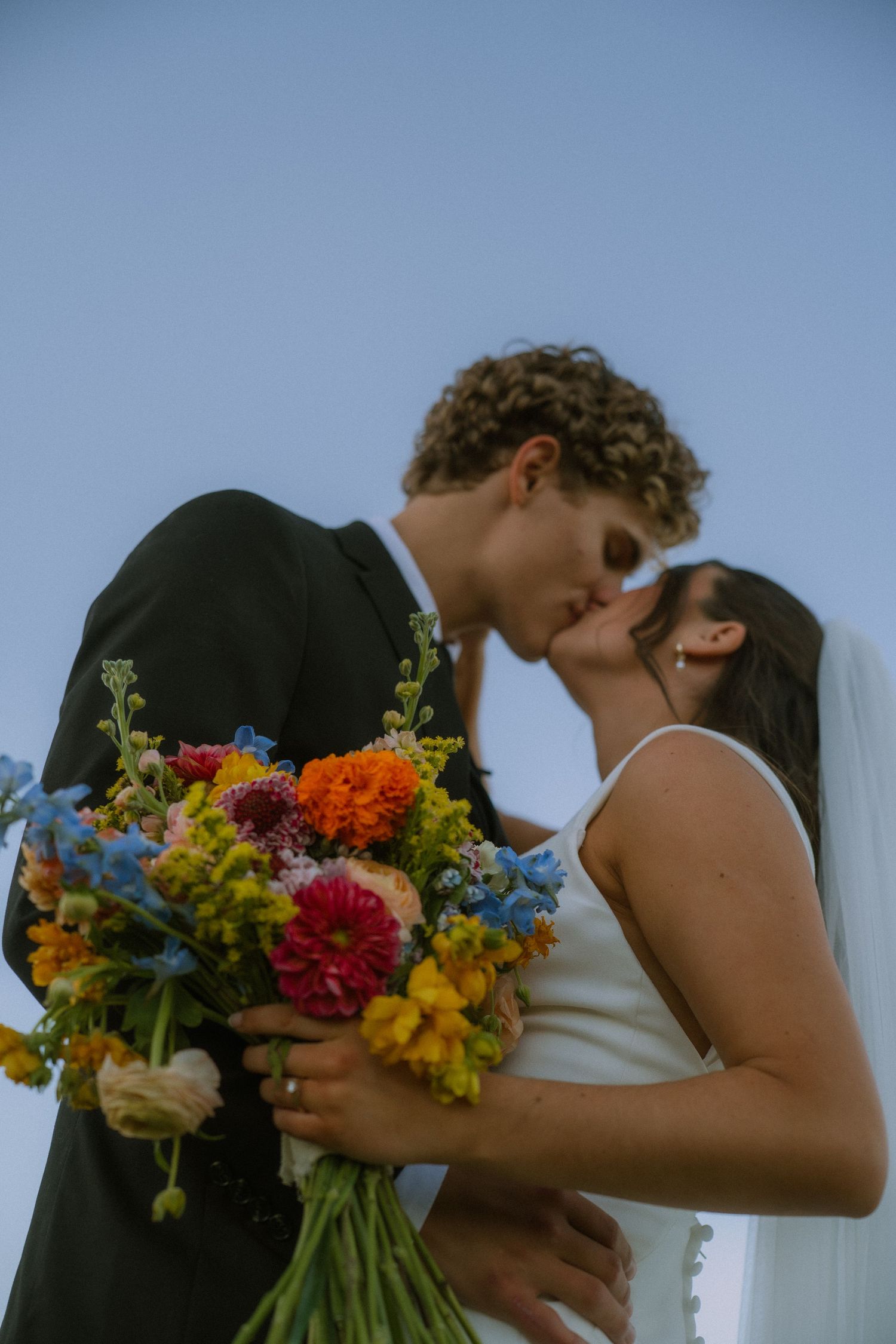 A wedding couple shares an intimate moment with a vibrant wildflower bouquet.