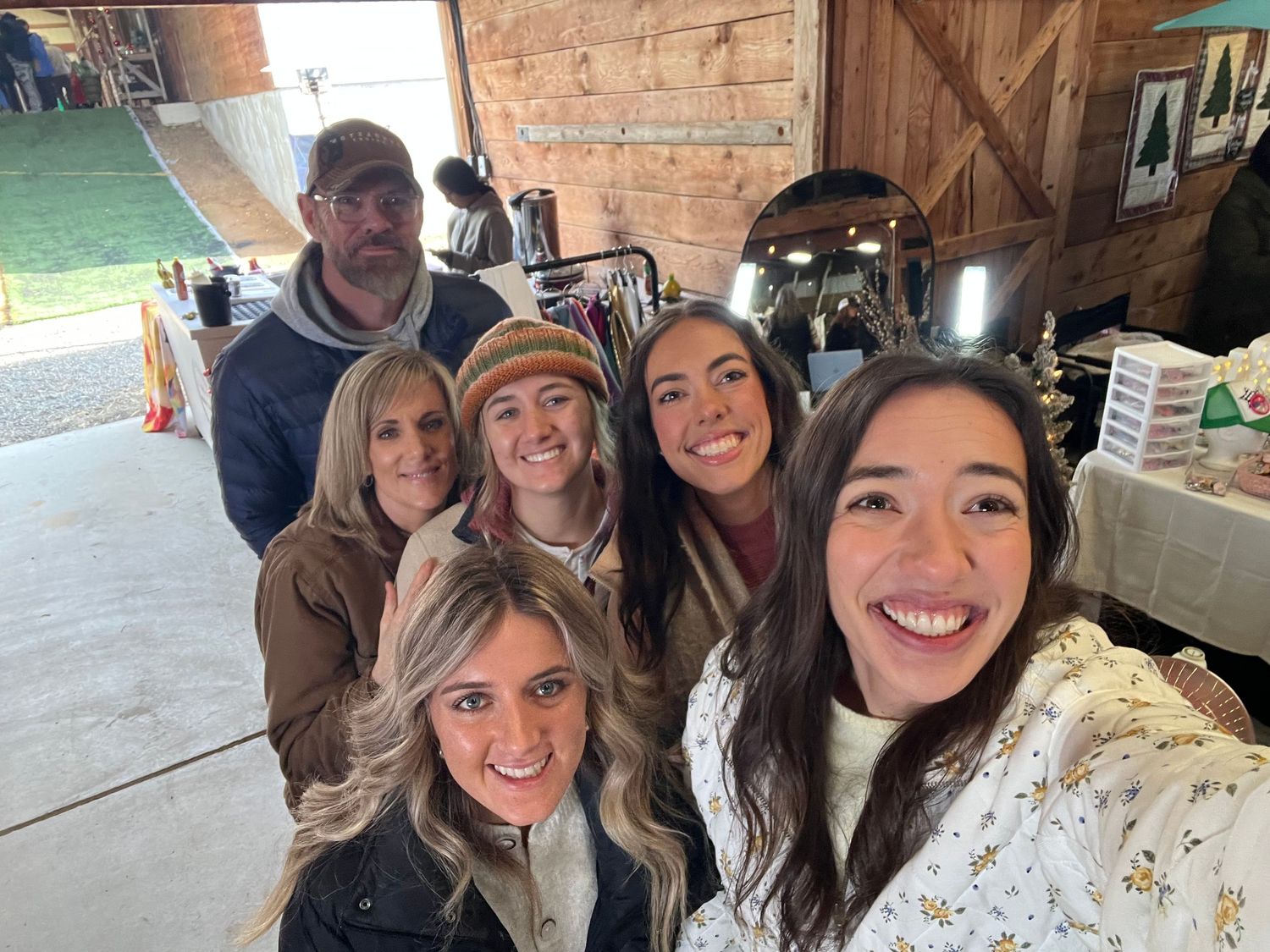 A group of friends smiling and taking selfies together at a rustic indoor location.
