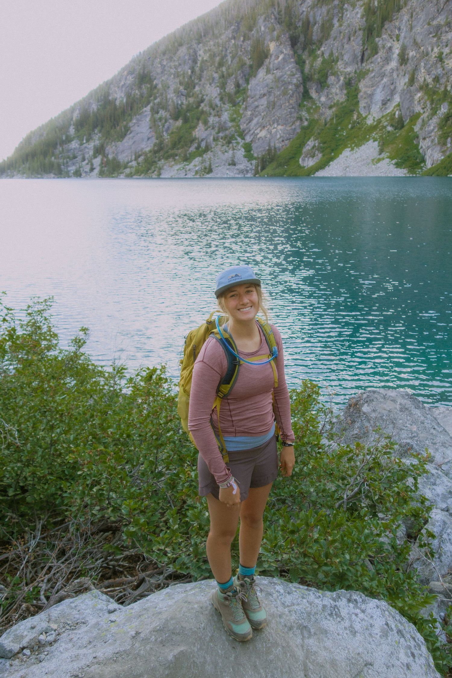 A hiker enjoys scenic views of turquoise alpine lake waters surrounded by steep rocky cliffs and green vegetation.
