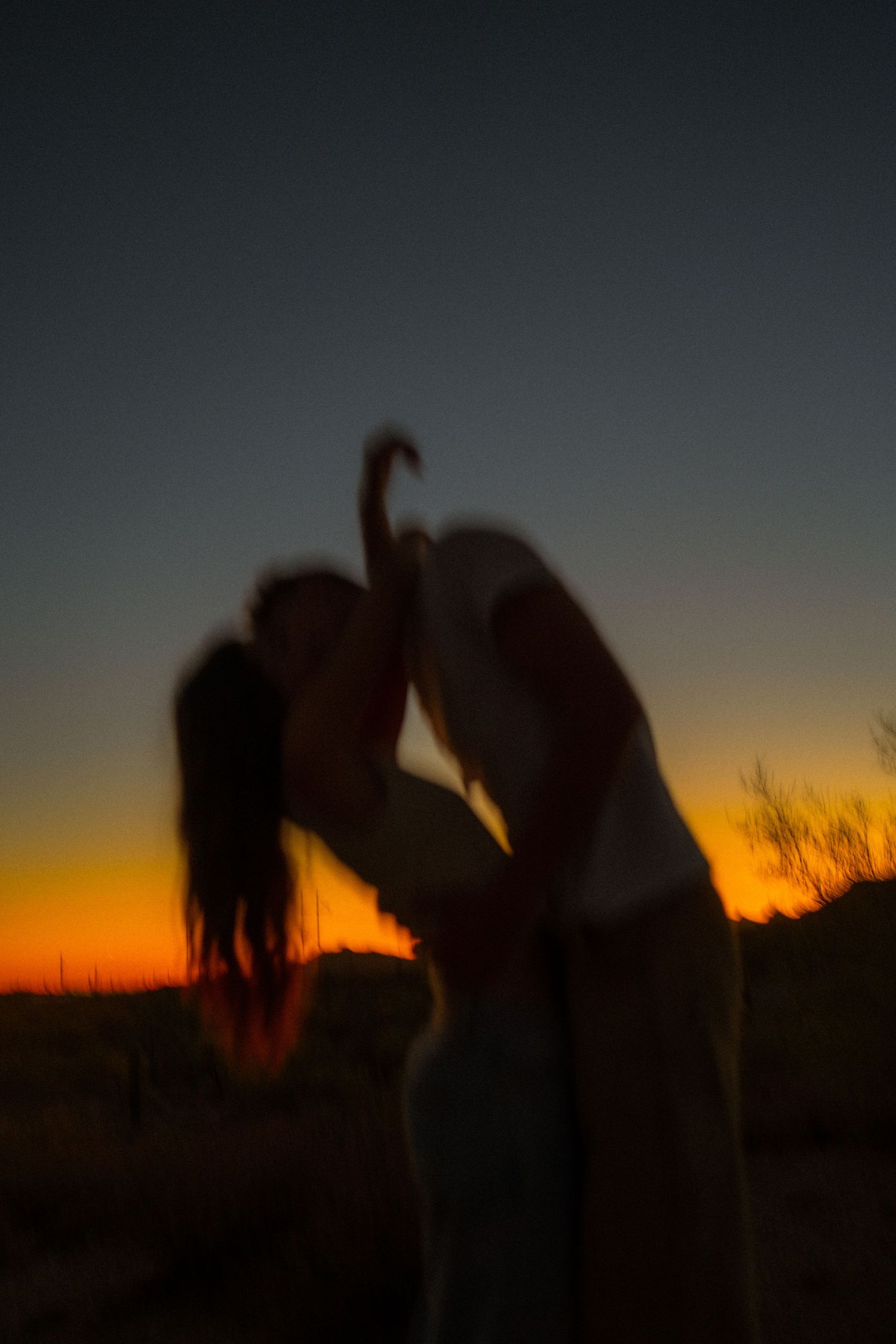 Silhouettes of people stand against a dramatic orange and blue sunset sky with dark landscape in foreground.