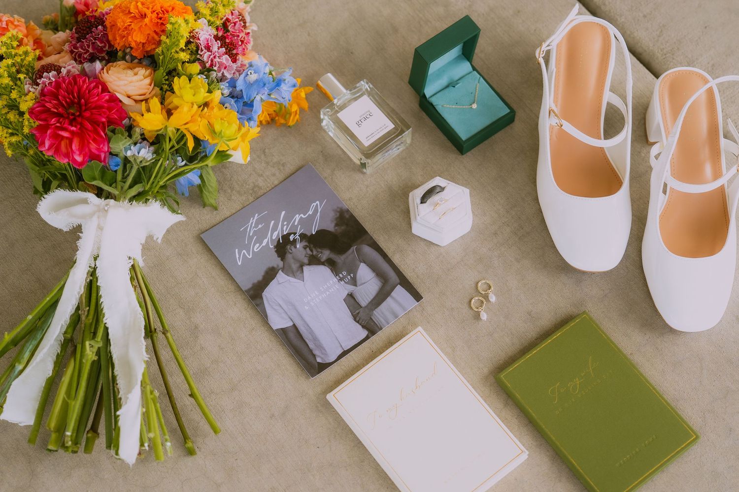 Wedding details including colorful flowers, white shoes, and green invitation cards arranged on a beige surface.