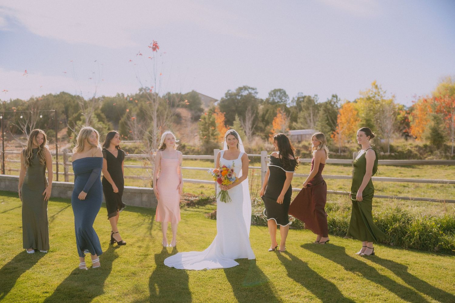 A wedding party walks through a sunlit autumn field casting long shadows during golden hour at sunset.