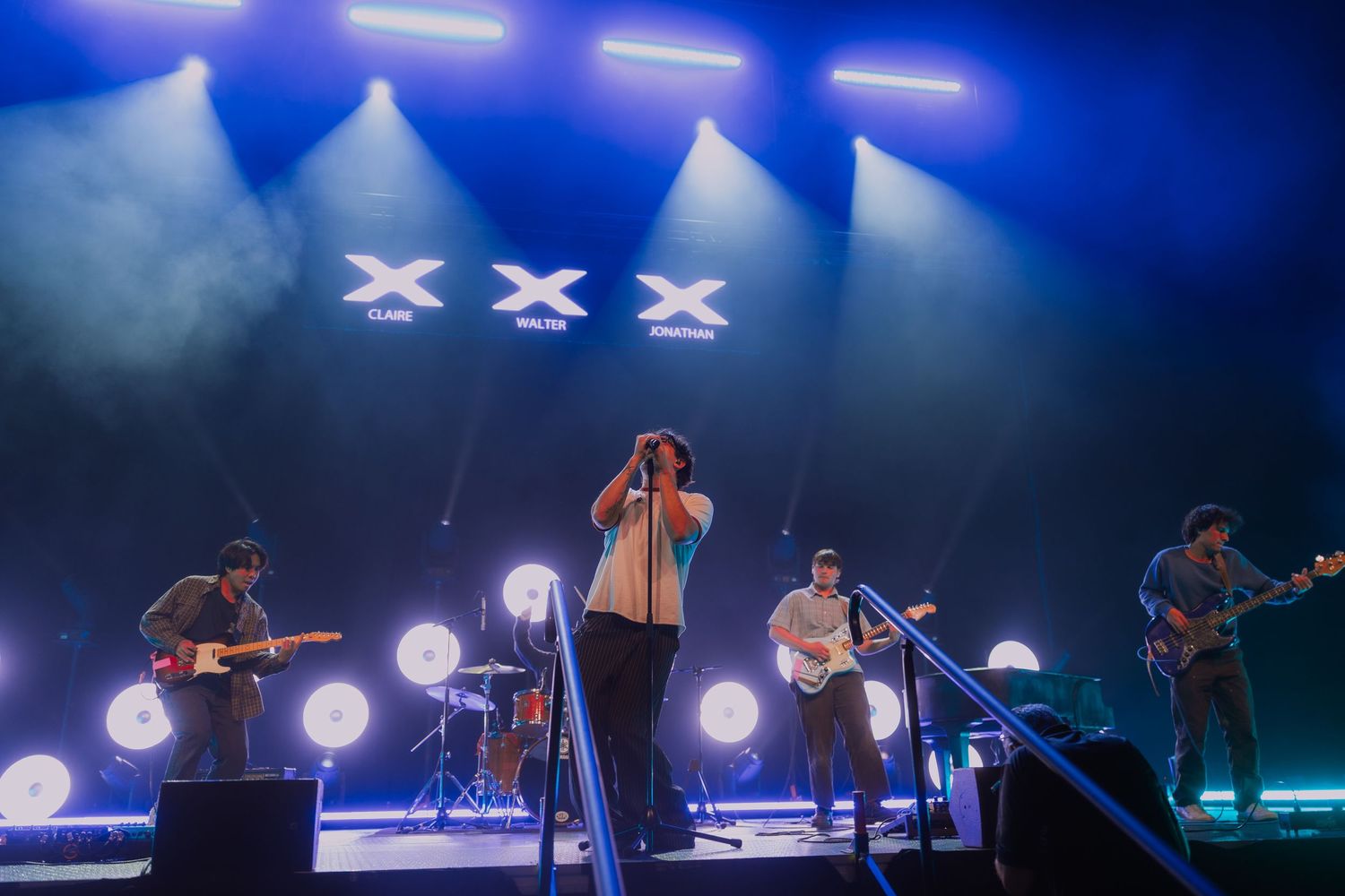 Silhouettes of performers on stage with dramatic blue lighting and spotlights during a concert performance.