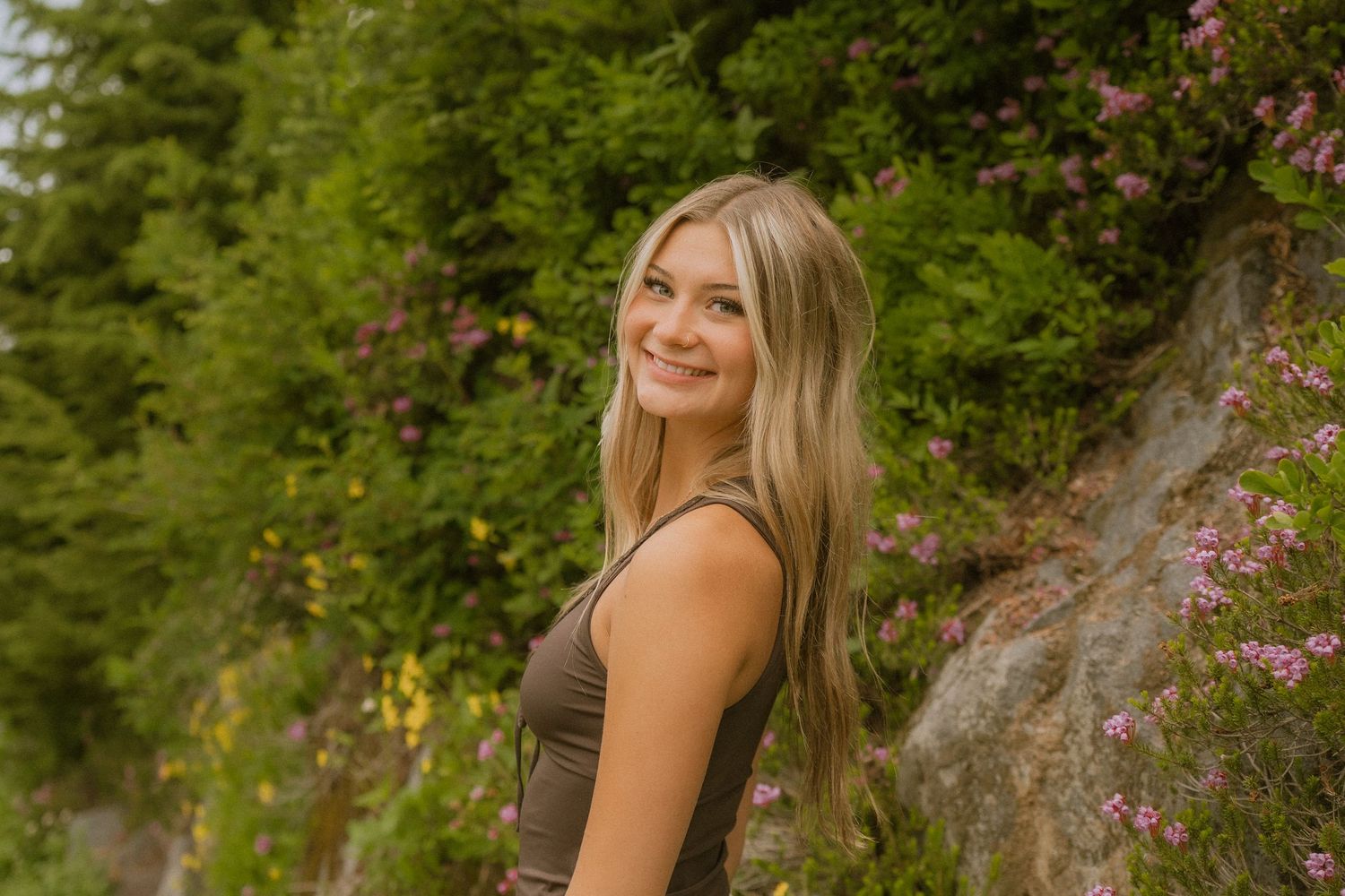 A senior portrait session in a lush garden setting with pink flowers and natural greenery in the background.