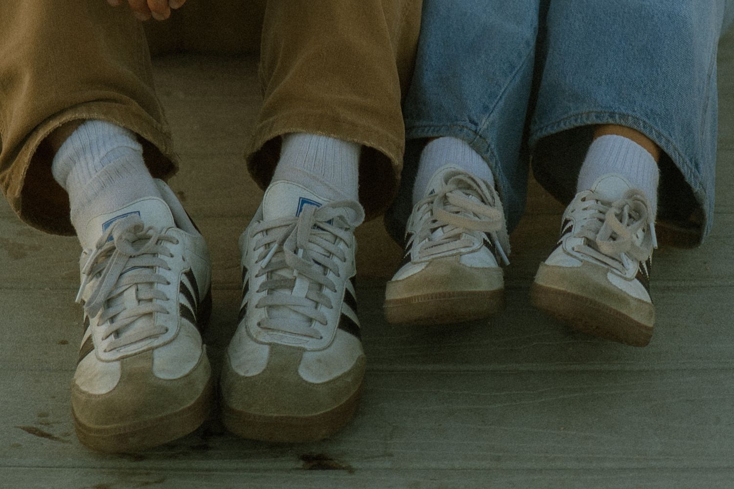 A row of feet wearing various casual shoes and sneakers lined up against a wall.