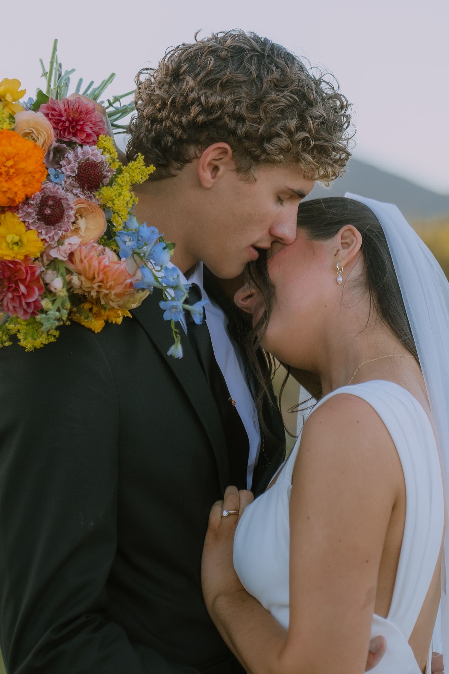 Wedding couple sharing intimate moment with vibrant wildflower bouquet.