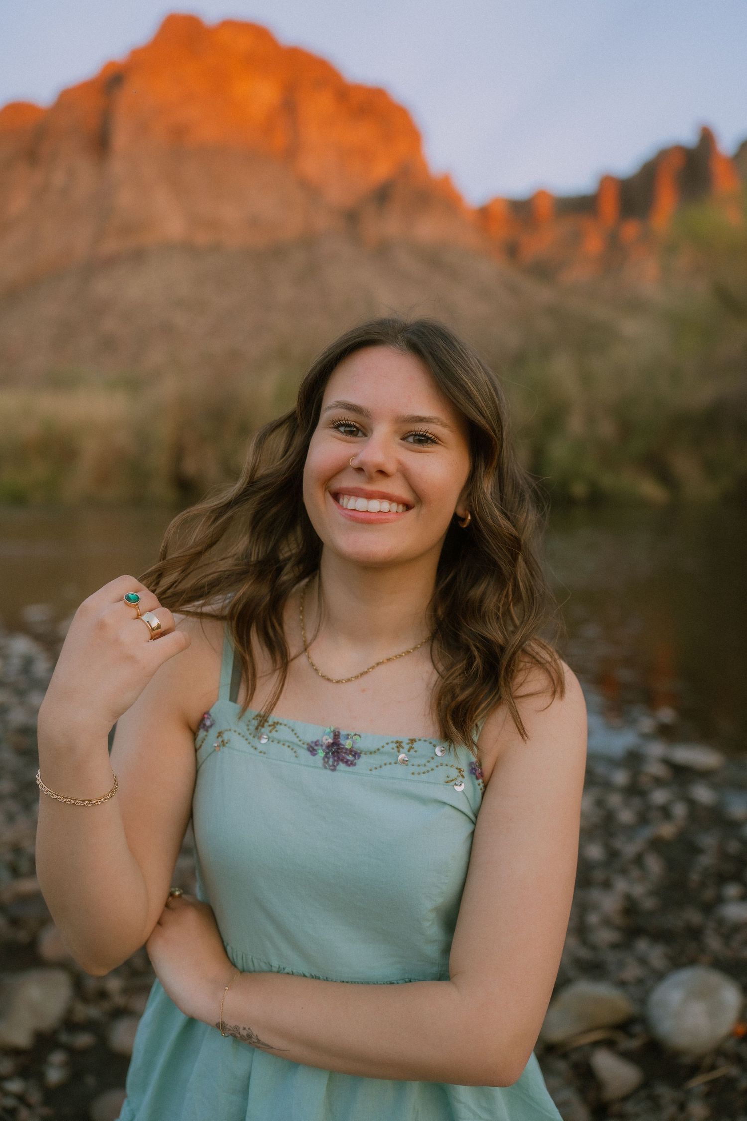 A person in a mint green top poses against a desert landscape with red rock formations at sunset.