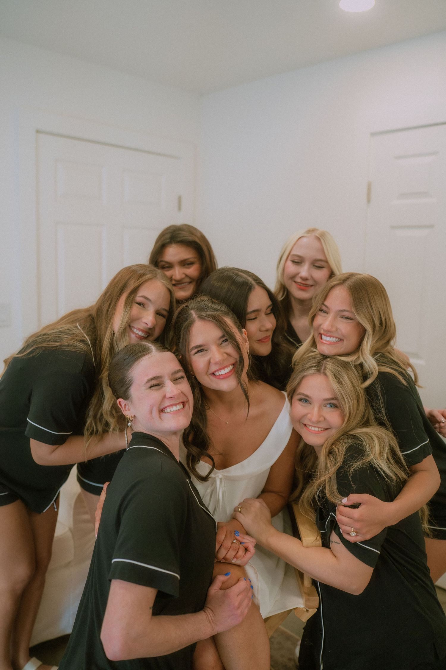 A group of friends in black and white outfits share joyful embraces and laughter together indoors.