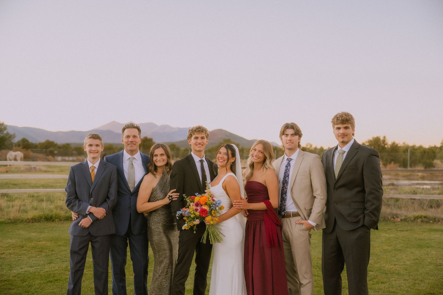 Wedding party poses together outdoors in burgundy and gray attire during fall season.