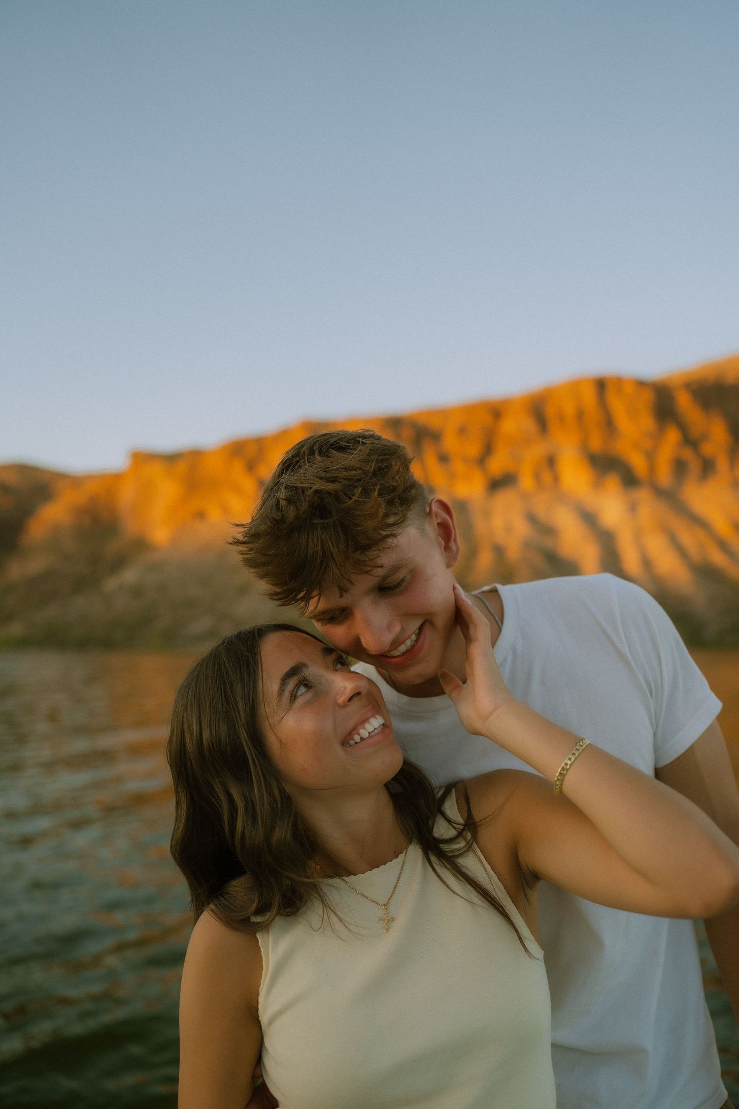 A couple shares a tender moment at sunset with mountains glowing orange in the background.