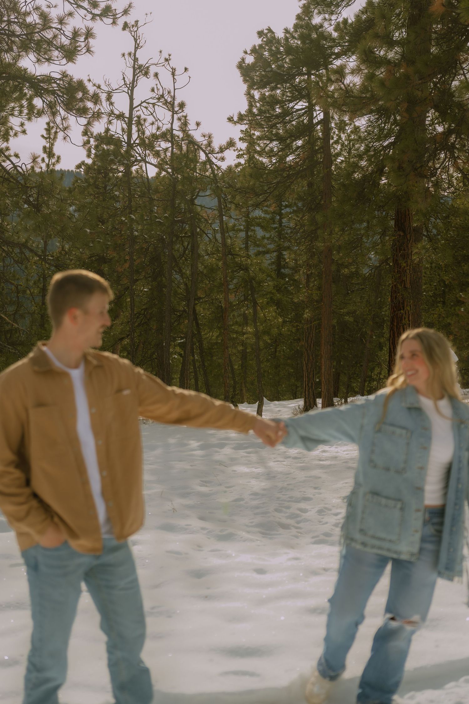 Two people in casual winter attire playfully throwing snowballs at each other in a snowy forest setting.