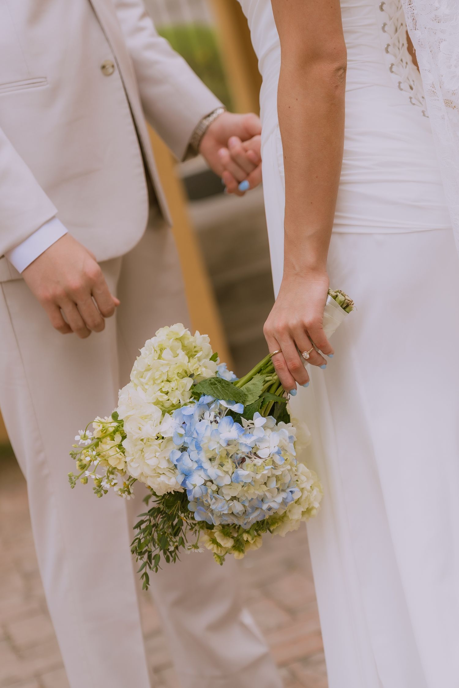 Row of bridesmaids in white dresses holding delicate bouquets of blue and white hydrangeas at an elegant wedding ceremony.