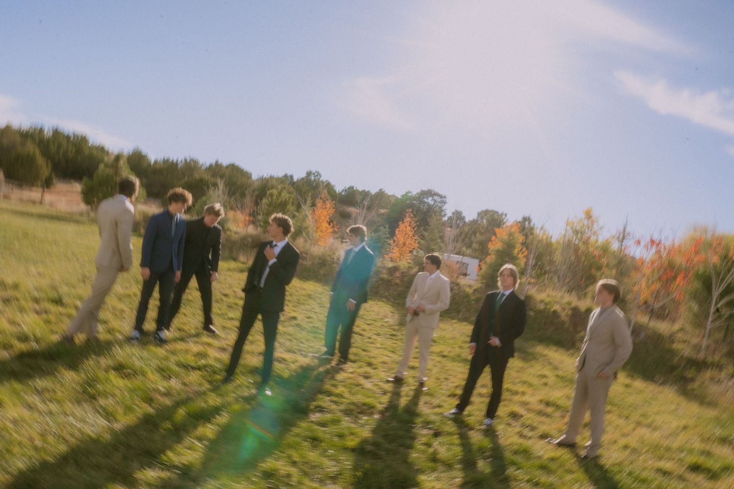 Wedding guests stand together casting long shadows on grass during golden hour.