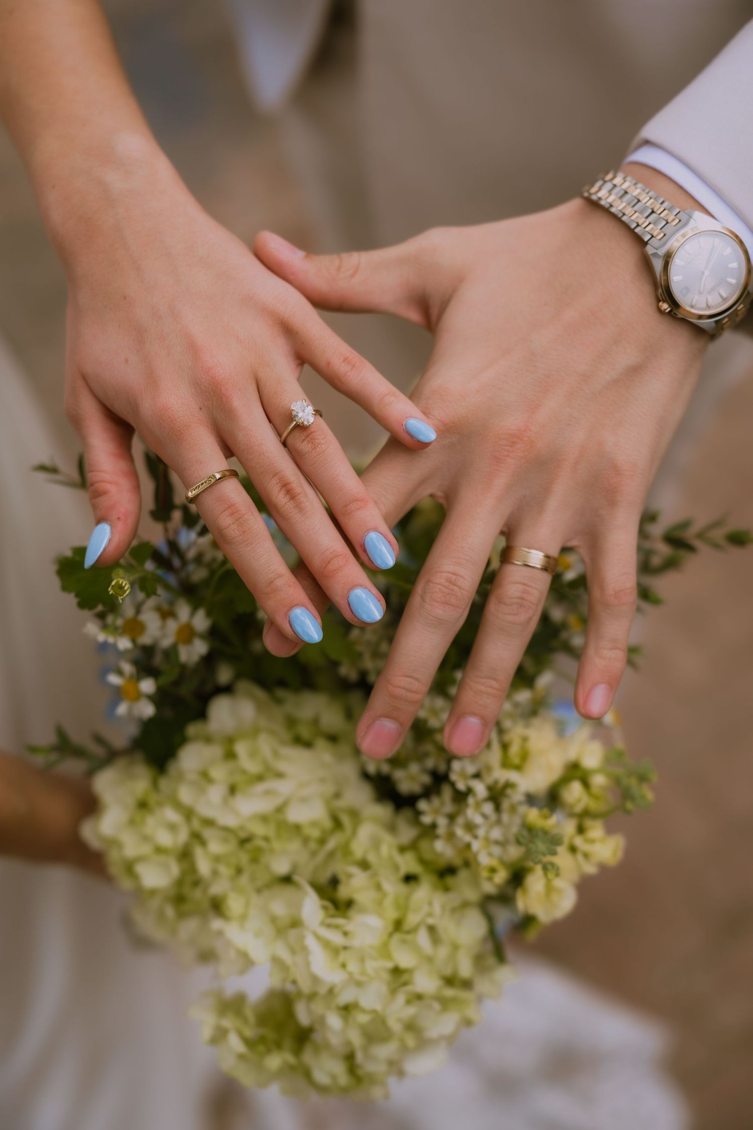 Hands with light blue nail polish and wedding rings delicately arrange white hydrangea flowers.