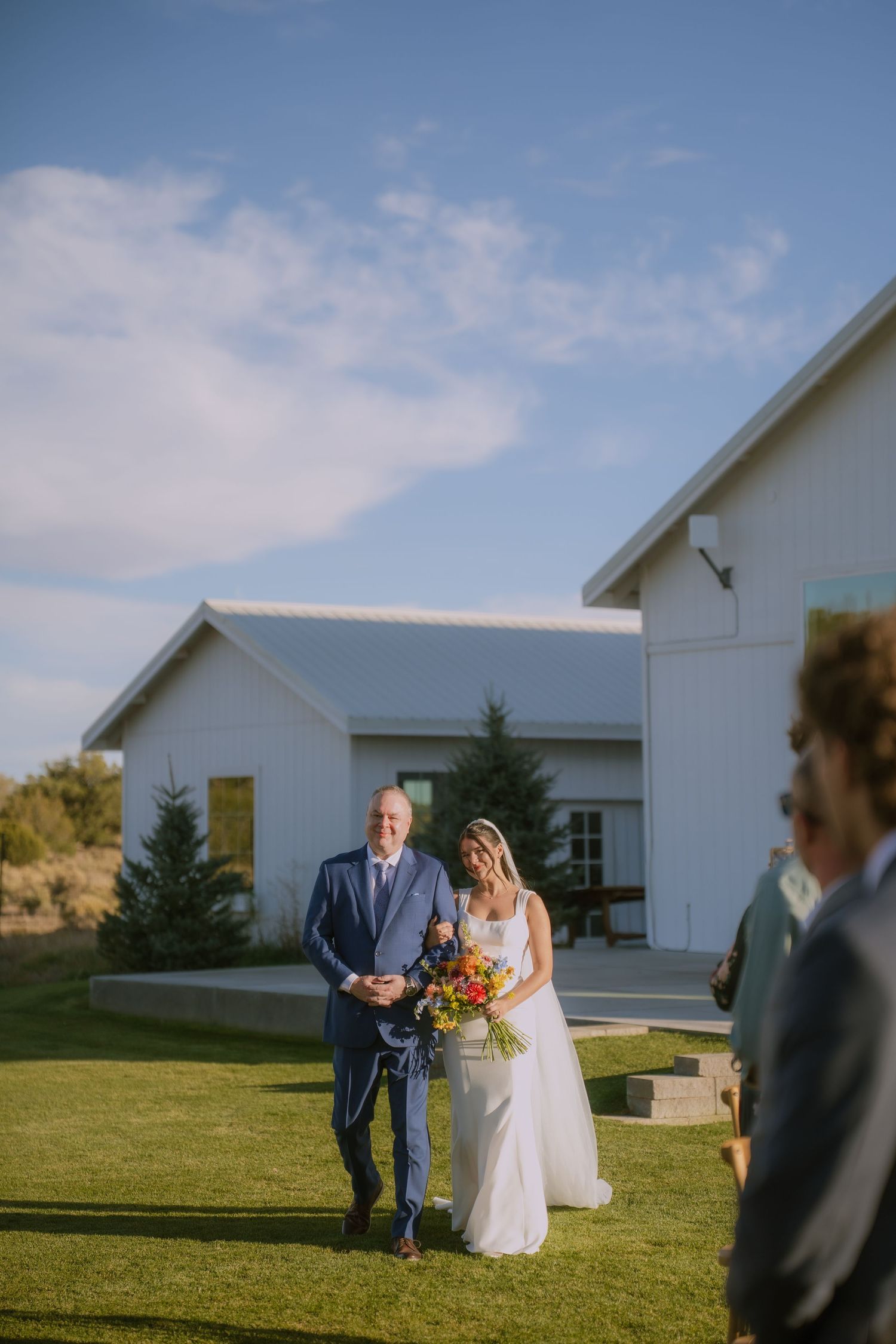 Outdoor wedding ceremony taking place in front of white buildings under blue skies.