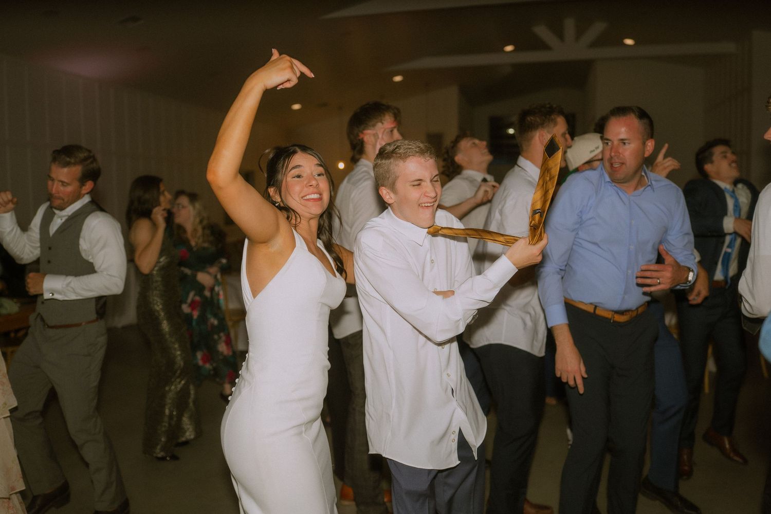 Wedding guests dancing and celebrating energetically on a dark reception dance floor.