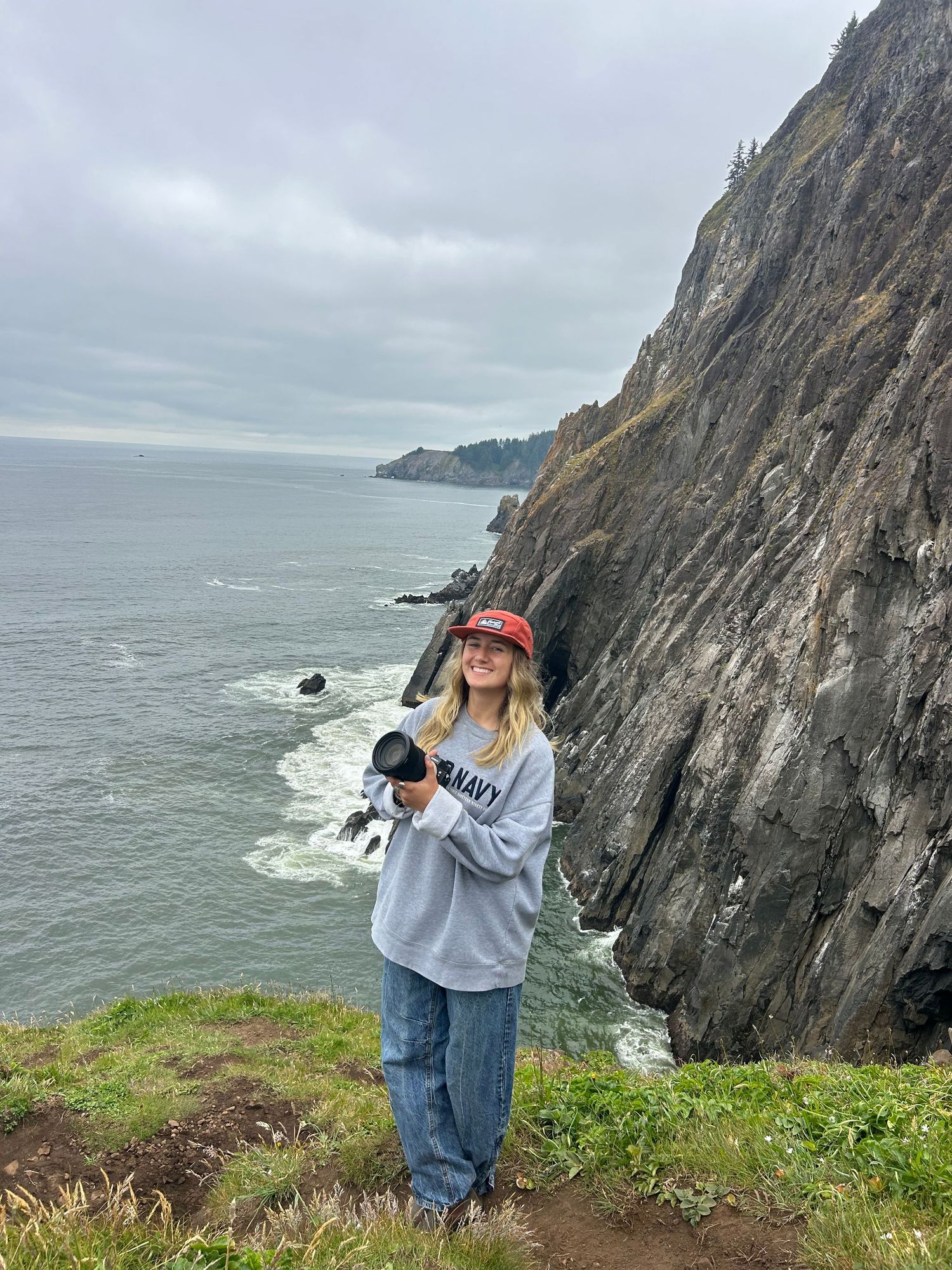 A photographer stands on a cliff edge overlooking dramatic coastal views at Slea Head Drive in Ireland.
