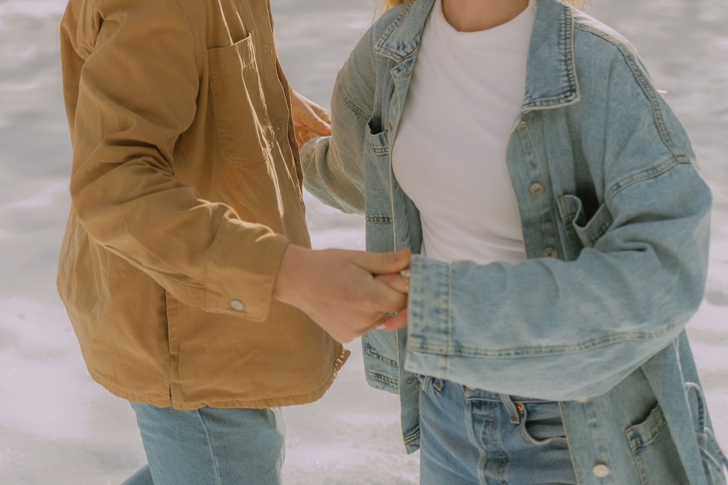 Two people in casual denim and brown outfits stand together in a light-filled setting.