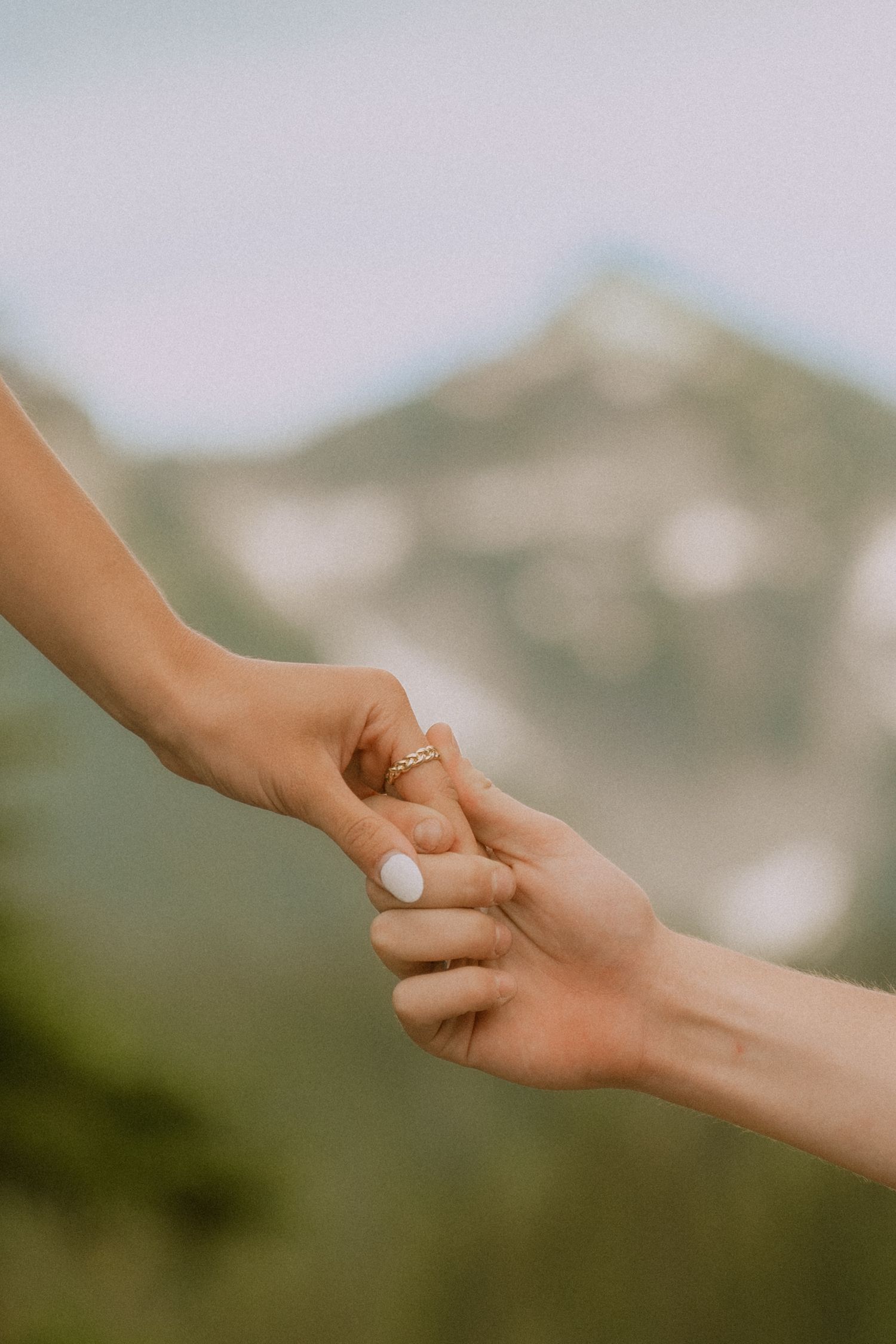 Close-up of hands holding each other against a blurred mountain landscape background.