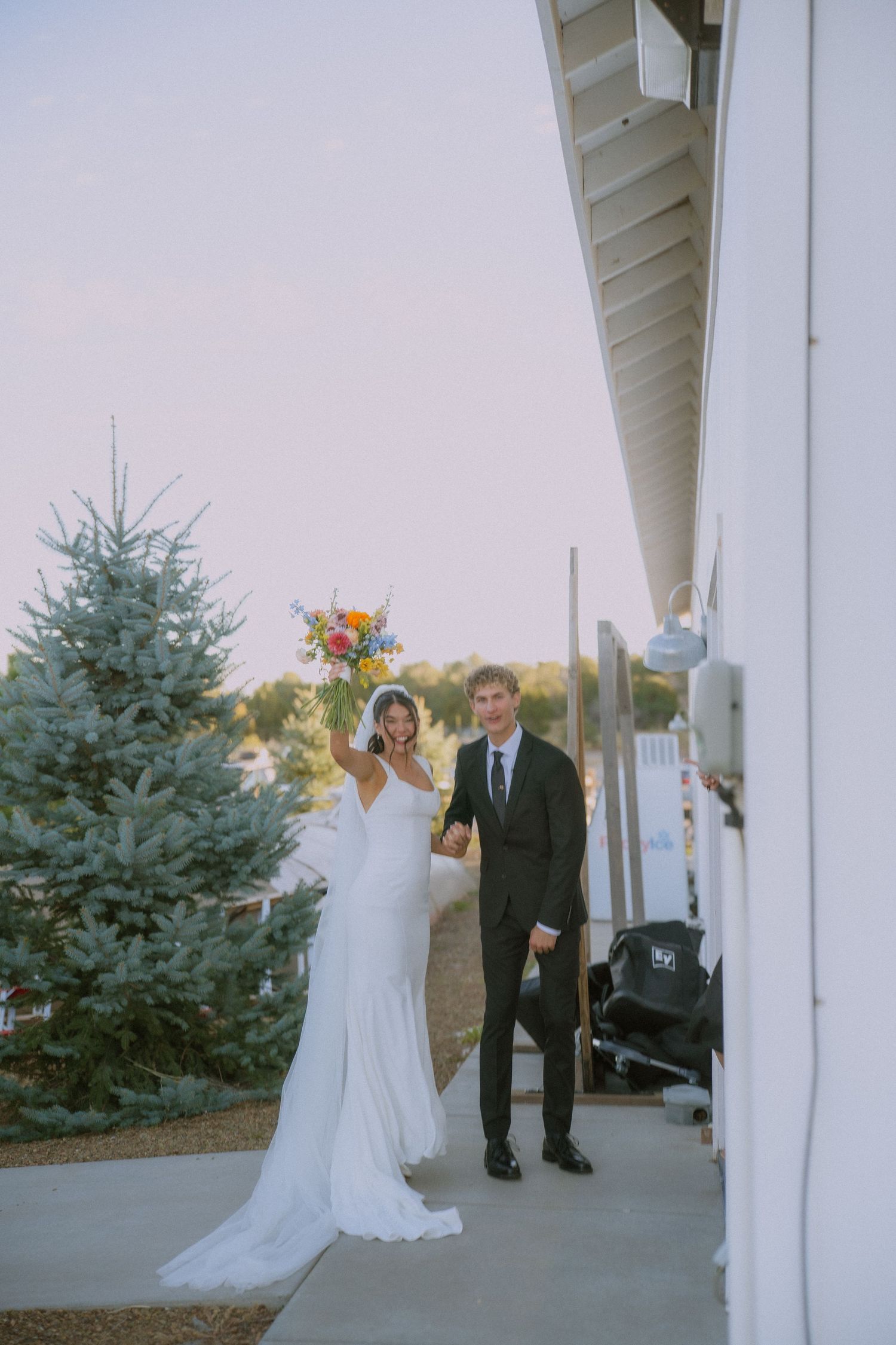 Wedding party members walk along the white exterior of a modern building.