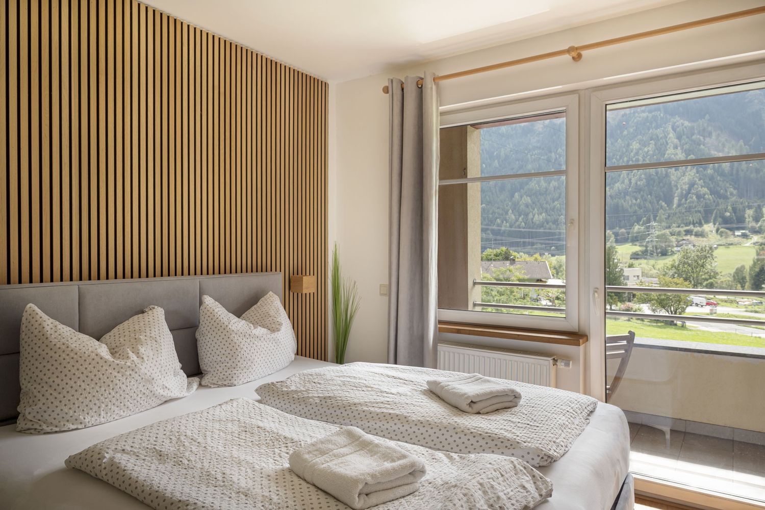 Ložnice s přímým vstupem na balkon v horském apartmánu. Pohodlná postel a možnost vyjít ven s výhledem na hory. Místo pro ranní kávu.