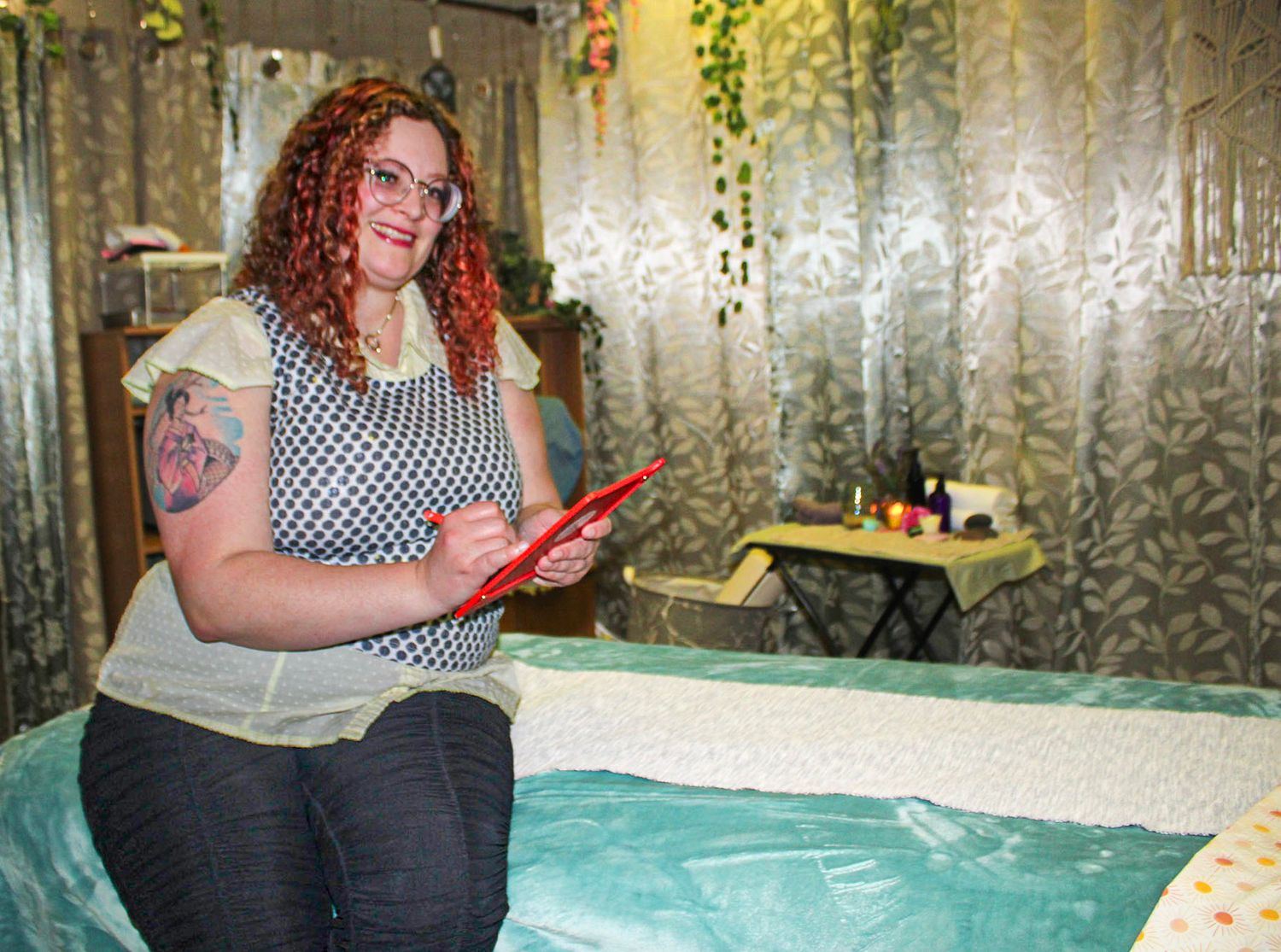 Woman with red curly hair holding a red clipboard sits on a massage table in a spa treatment room.