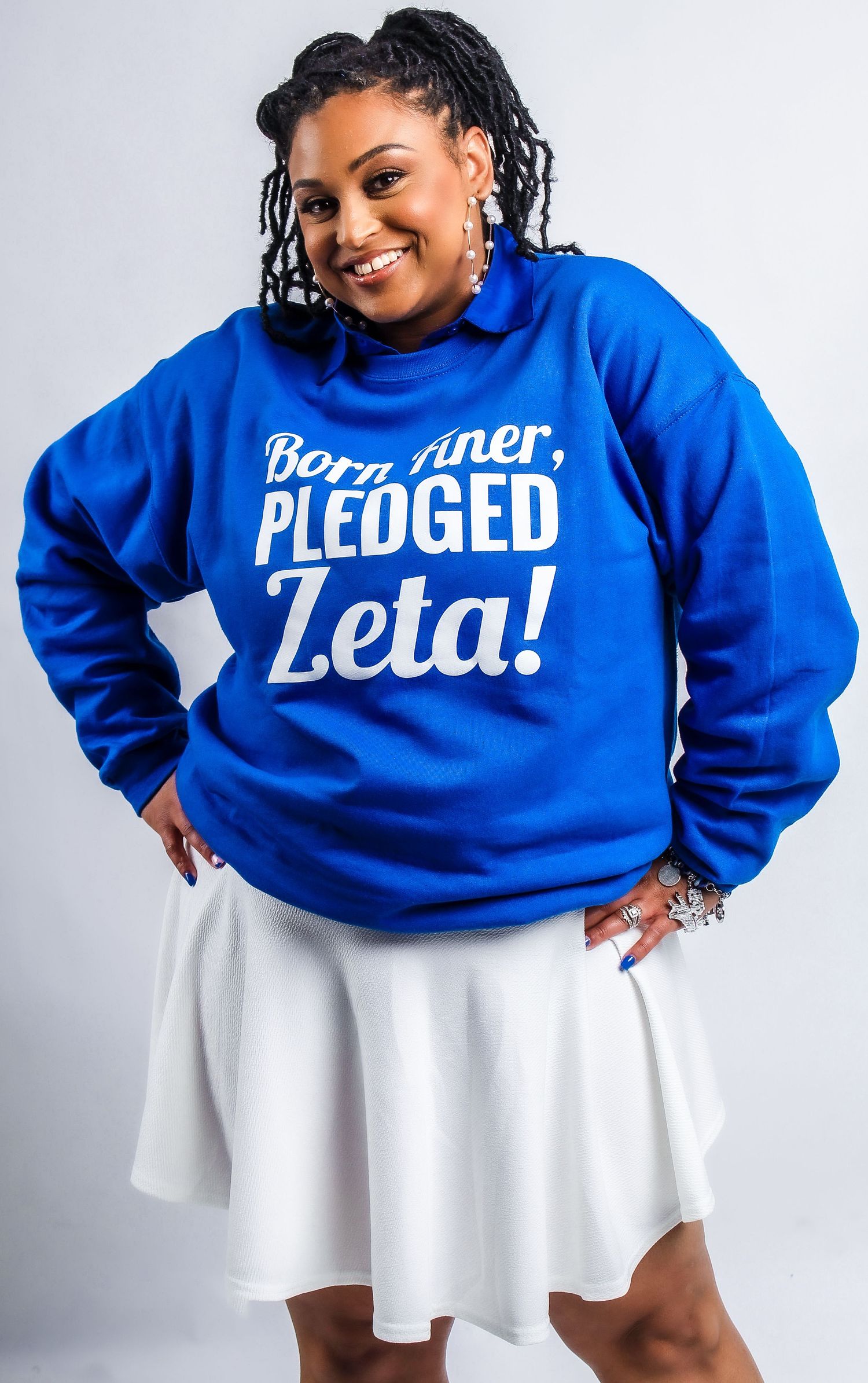 Person in blue Zeta sweatshirt and white skirt posing against white background.