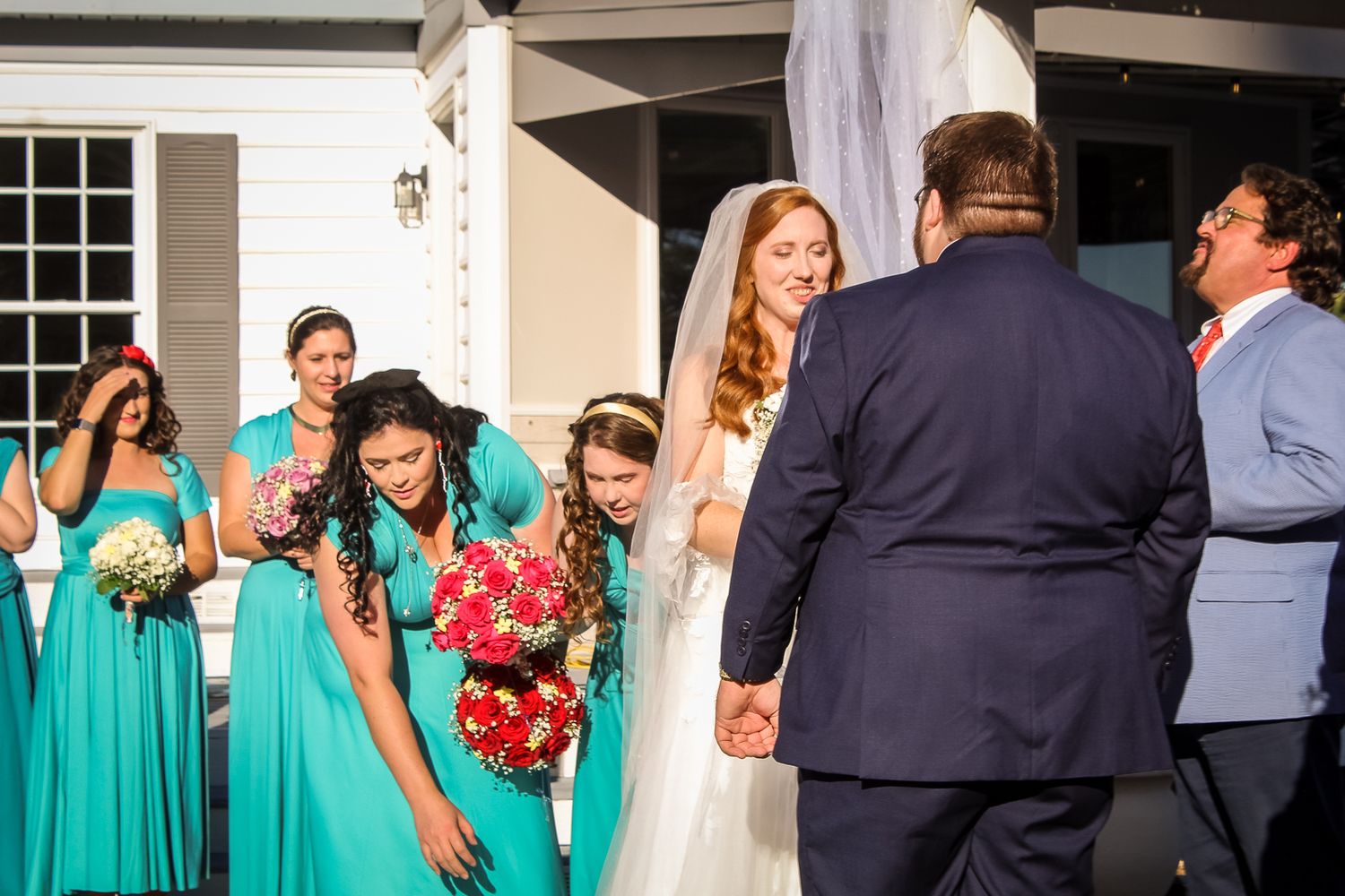 Bride in white gown with bridesmaids in teal dresses holding bouquets outside a church on wedding day.