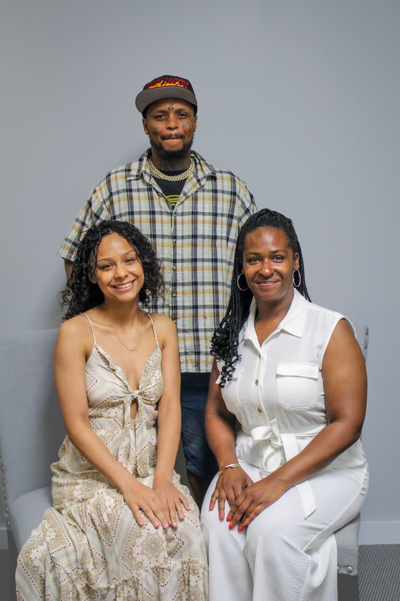 Three people posing for a portrait, two women seated and a man standing, against a light gray background.
