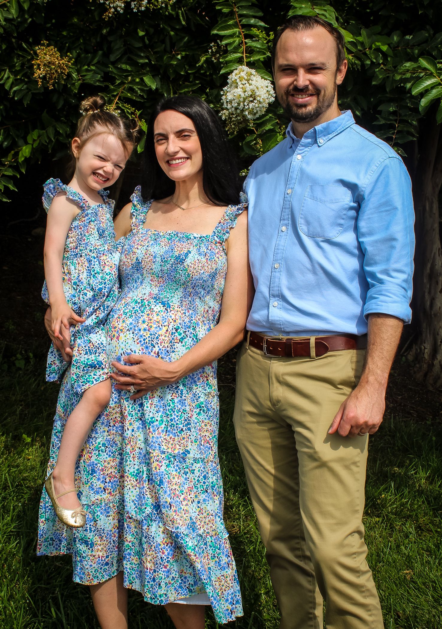 A family poses outdoors in coordinated blue outfits, with a floral sundress and light blue button-down shirt.
