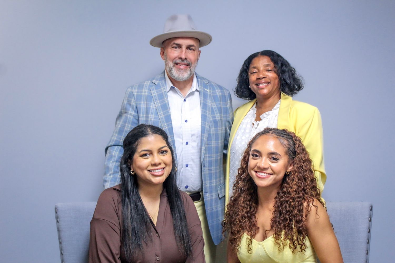 Four smiling people pose together for a group portrait against a light gray background in professional attire.