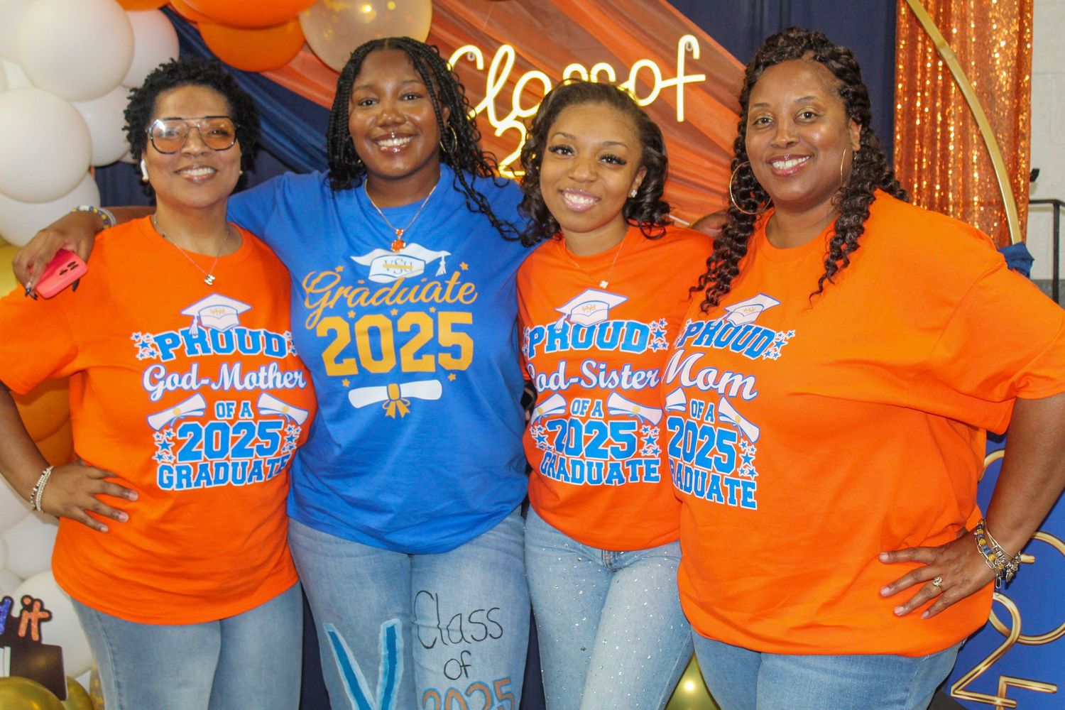 Four women in orange and blue Class of 2025 graduate shirts smile together at a graduation celebration party.