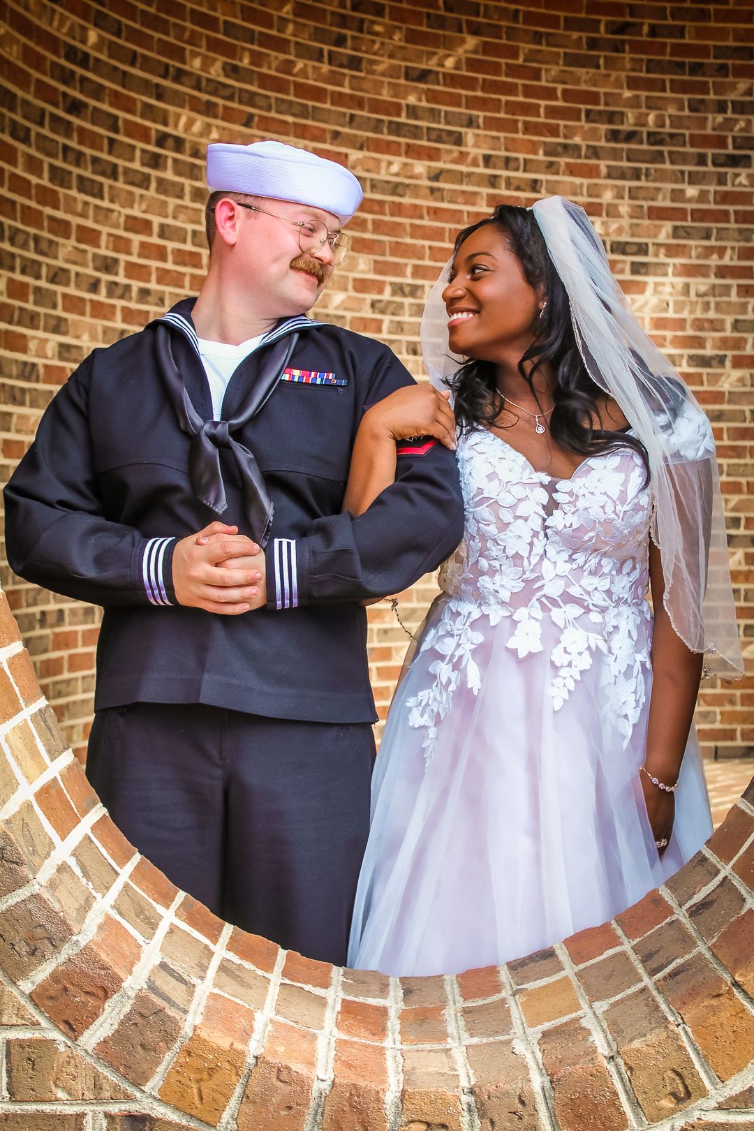 A series of romantic wedding photos showing a couple in navy military uniform and white lace dress against a brick wall.