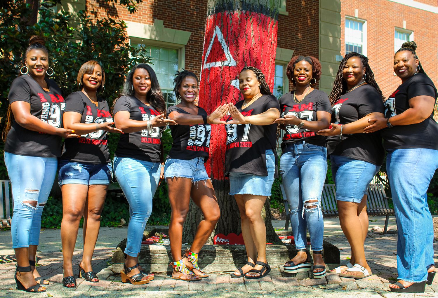 Group of women in matching black shirts posing outdoors, smiling and holding items near a colorful mural.