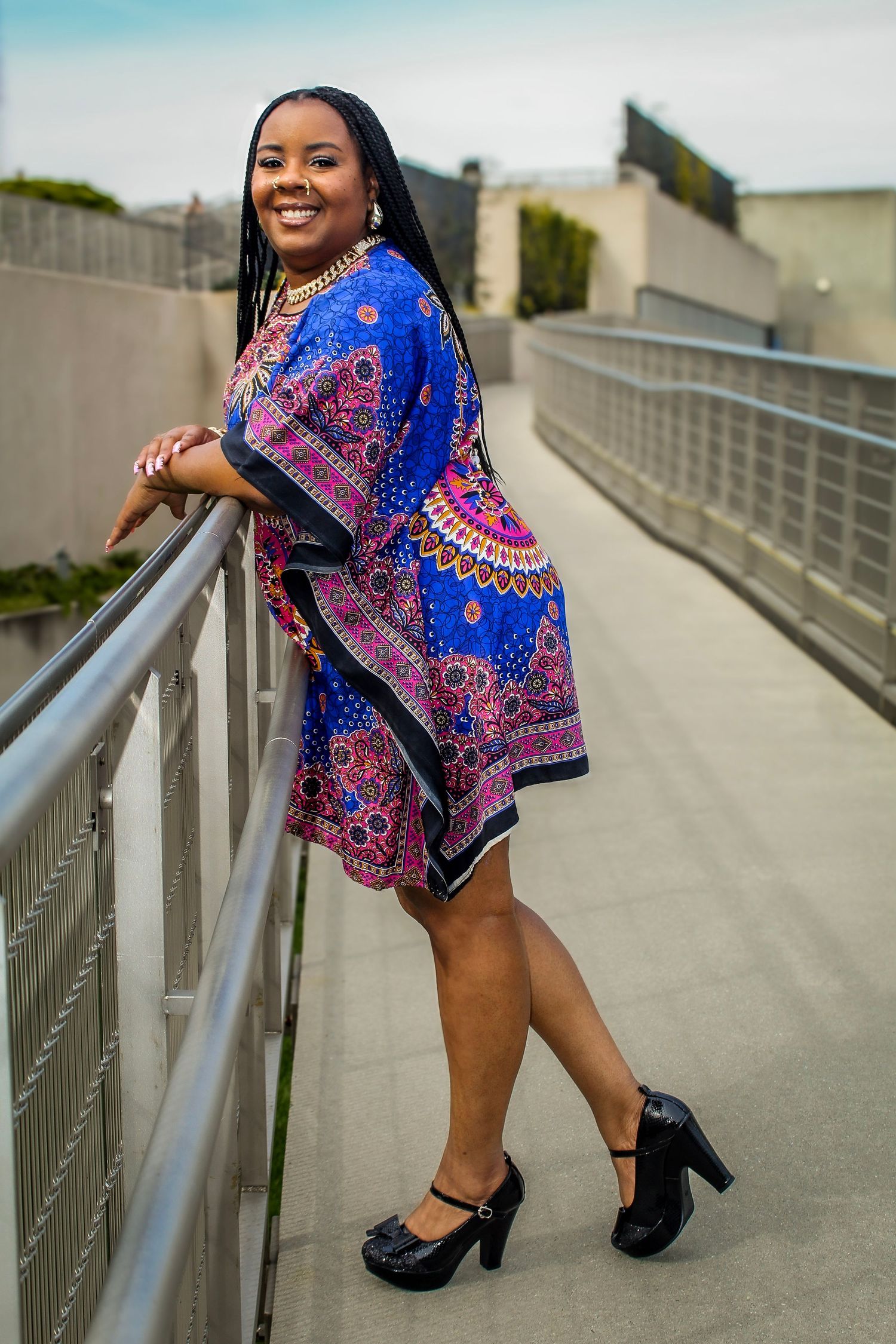 Person in vibrant blue patterned dress posing on concrete walkway with railing.
