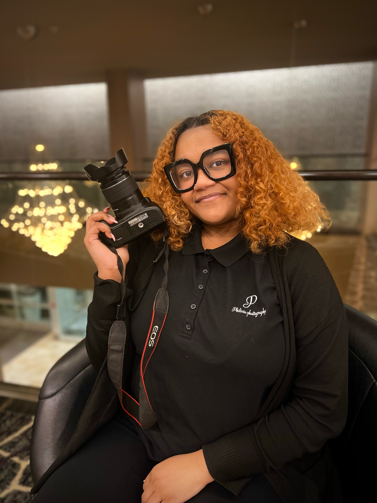 Professional photographer with curly hair and glasses holding camera in dark indoor setting.