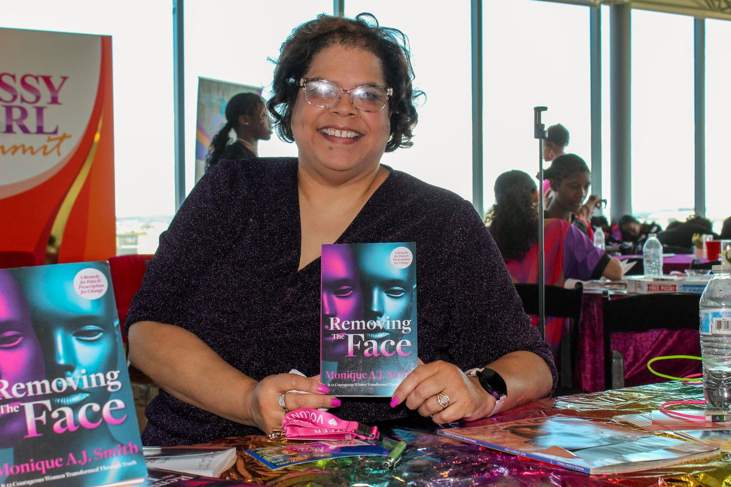 Author Monique A. Losier smiles holding her book Removing the Face at a book signing event.