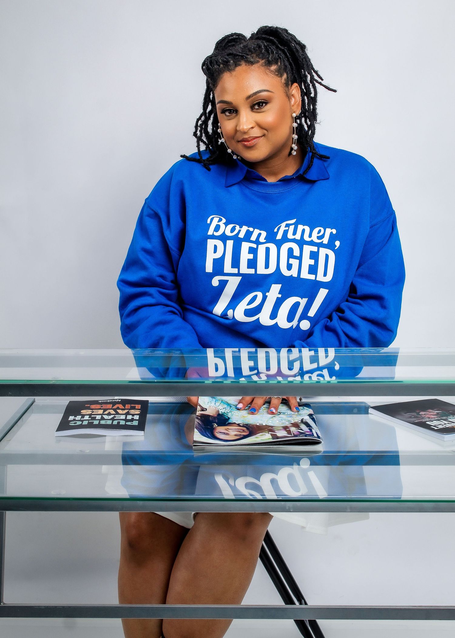 Person wearing blue sorority sweatshirt at desk with glass surface.