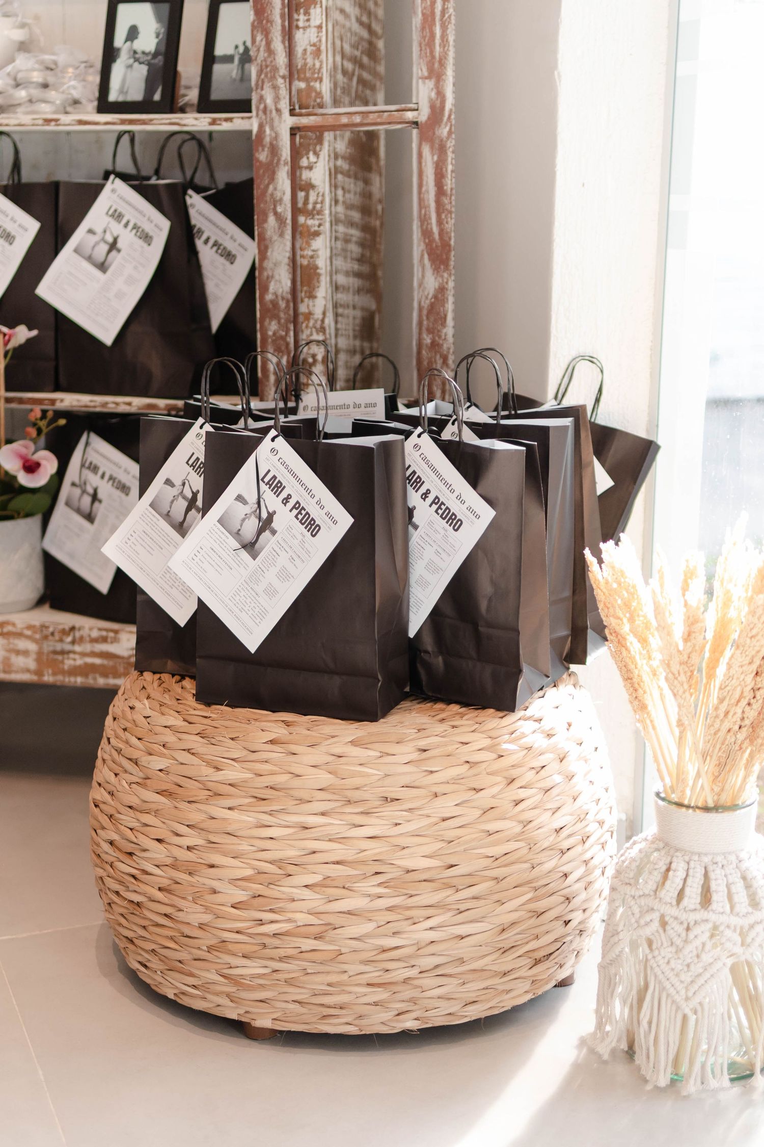 Black gift bags arranged in a display with white tags alongside a woven basket and decorative wheat stalks.