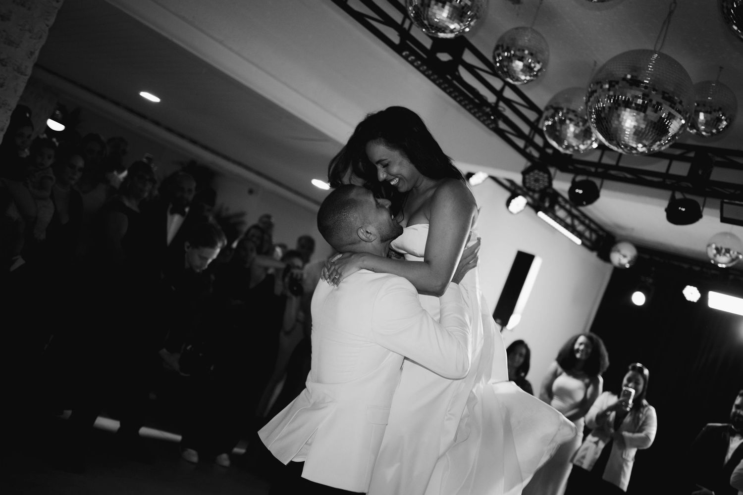 A dark reception venue with stage lighting and people dancing in silhouette.