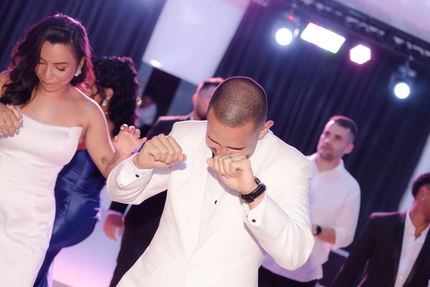 A couple dances together during a wedding reception with blue stage lighting in the background.