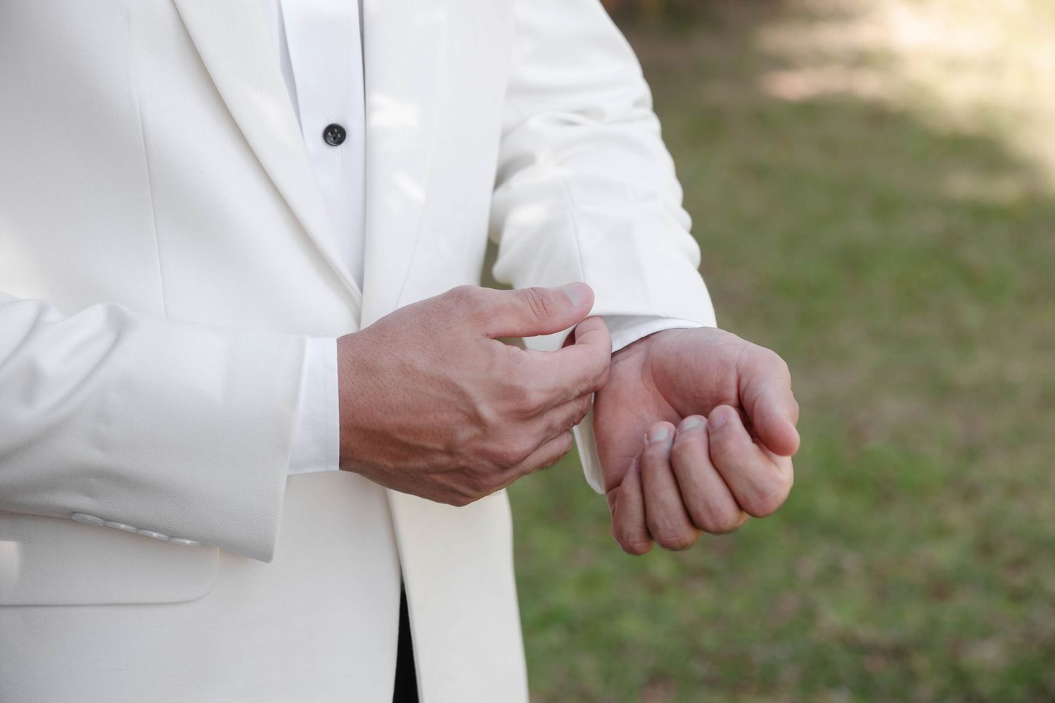 A person in a white suit jacket adjusts their cufflinks during a formal event.