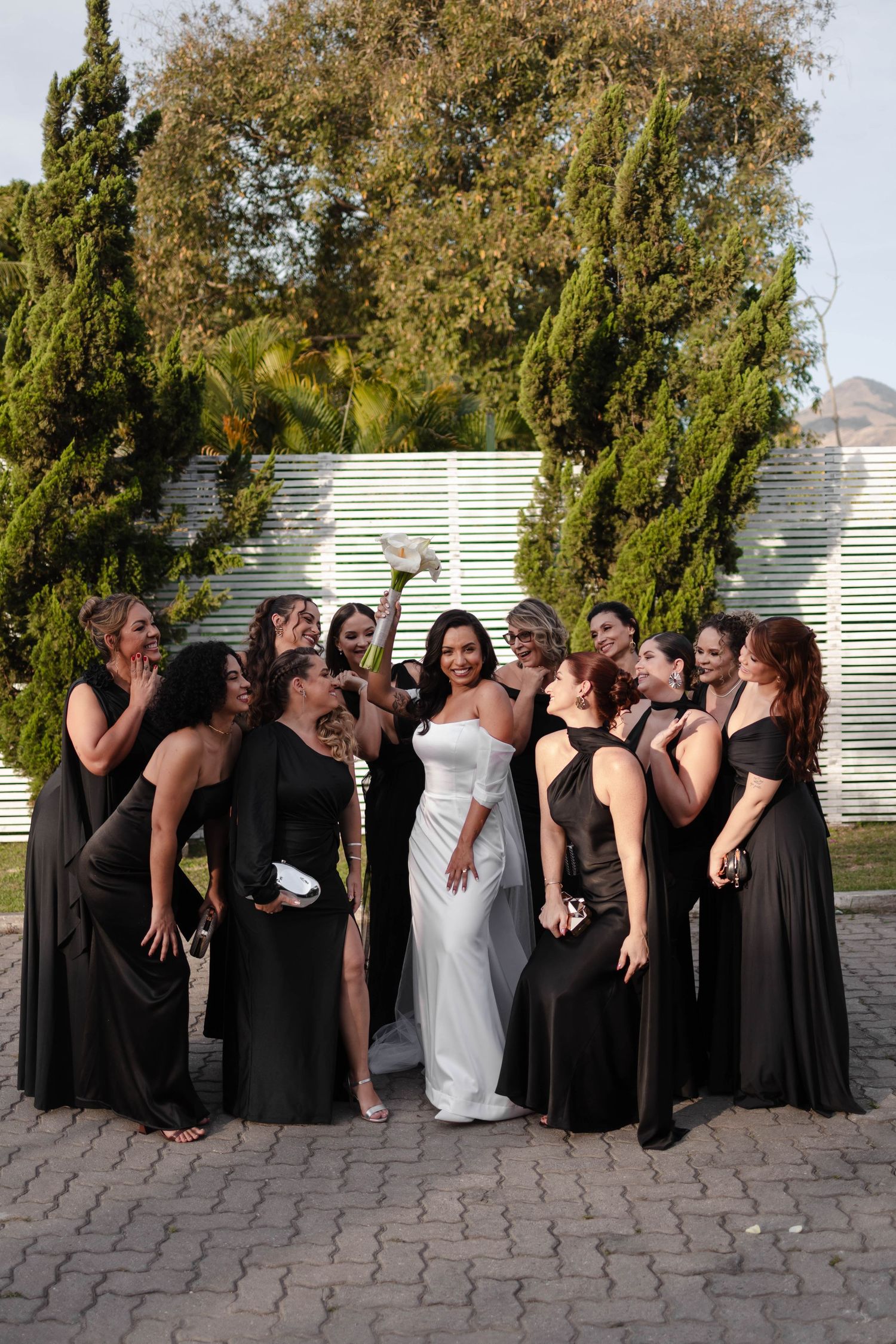 Wedding party in black dresses poses in sequence showing playful falling domino effect on stone patio.