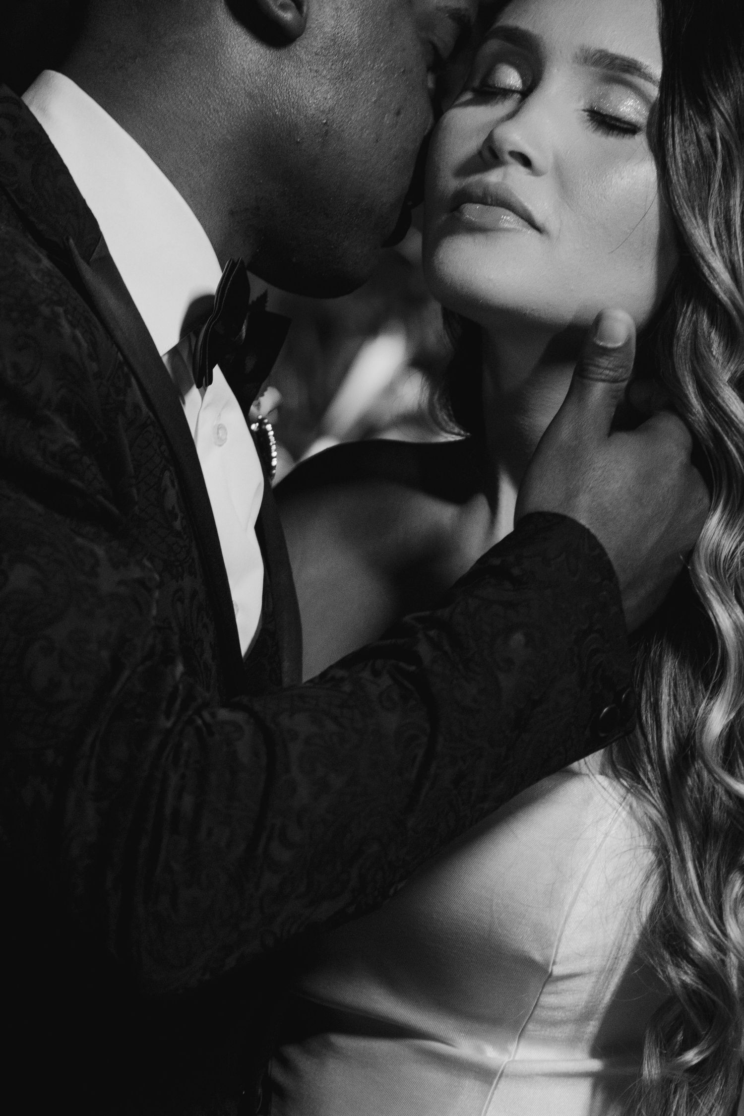 Intimate black and white portrait of a romantic couple in formal attire sharing a tender moment.