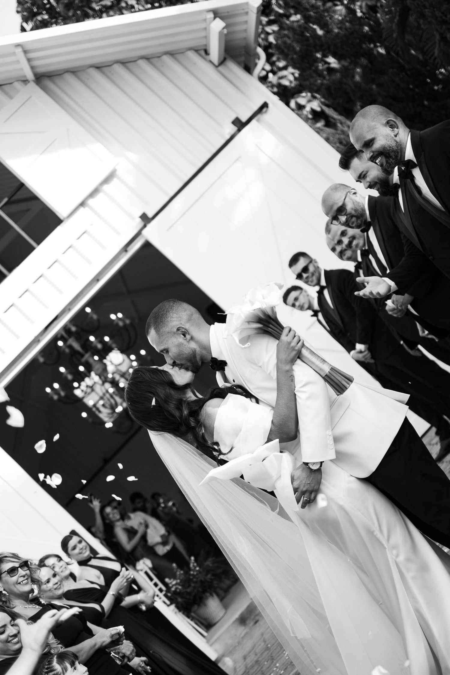A celebratory wedding kiss captured from below with confetti falling and guests cheering.