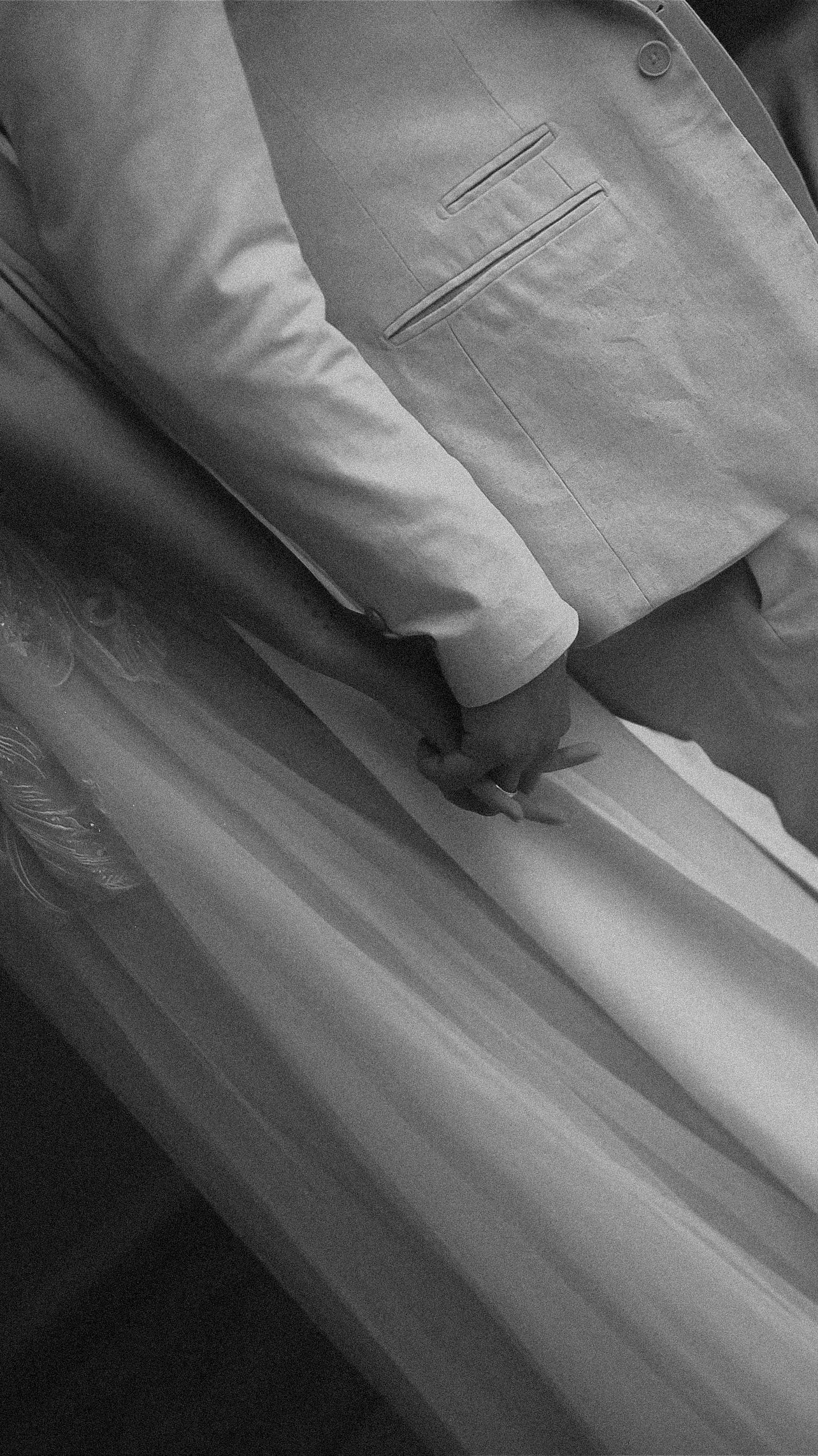 A close-up detail shot of hands touching white wedding dress fabric and formal attire.