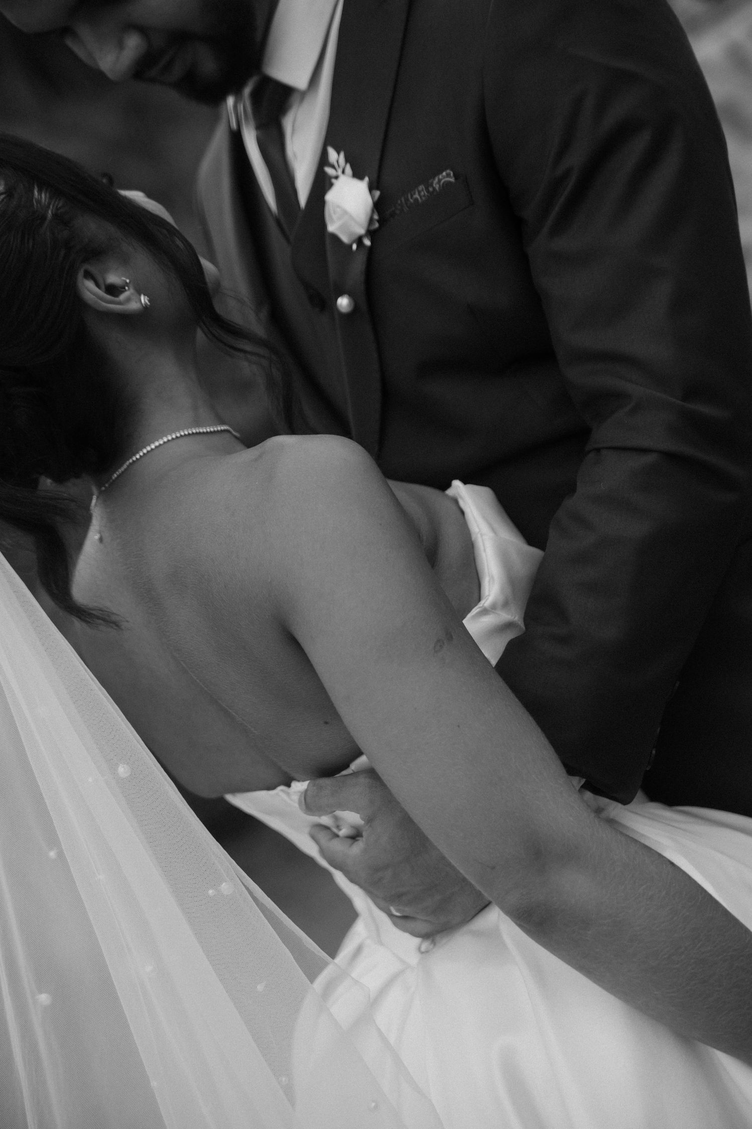 A black and white photograph showing a close-up of a couple in formal wedding attire sitting together.
