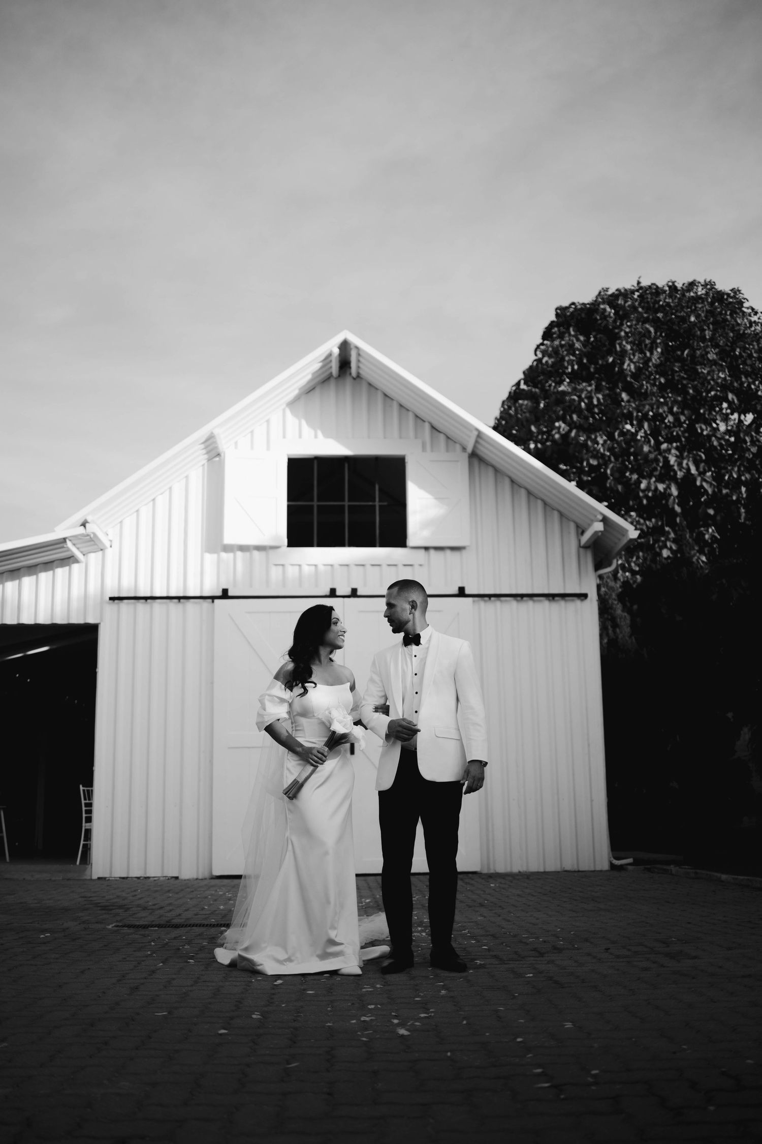 A black and white wedding sequence showing a couple dancing and dipping in front of a white barn building.
